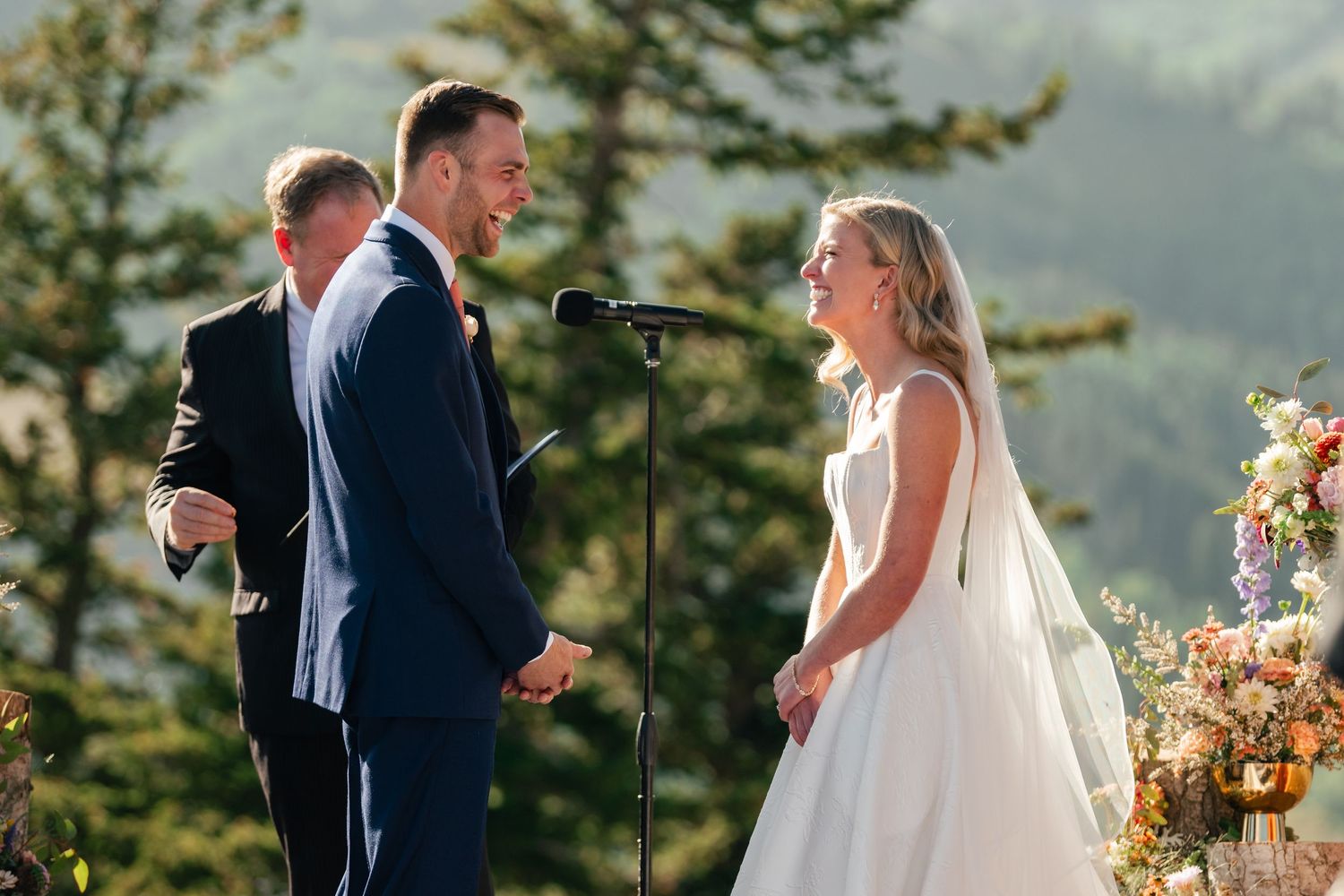 A couple exchanges vows during an outdoor mountain wedding ceremony surrounded by evergreen trees.