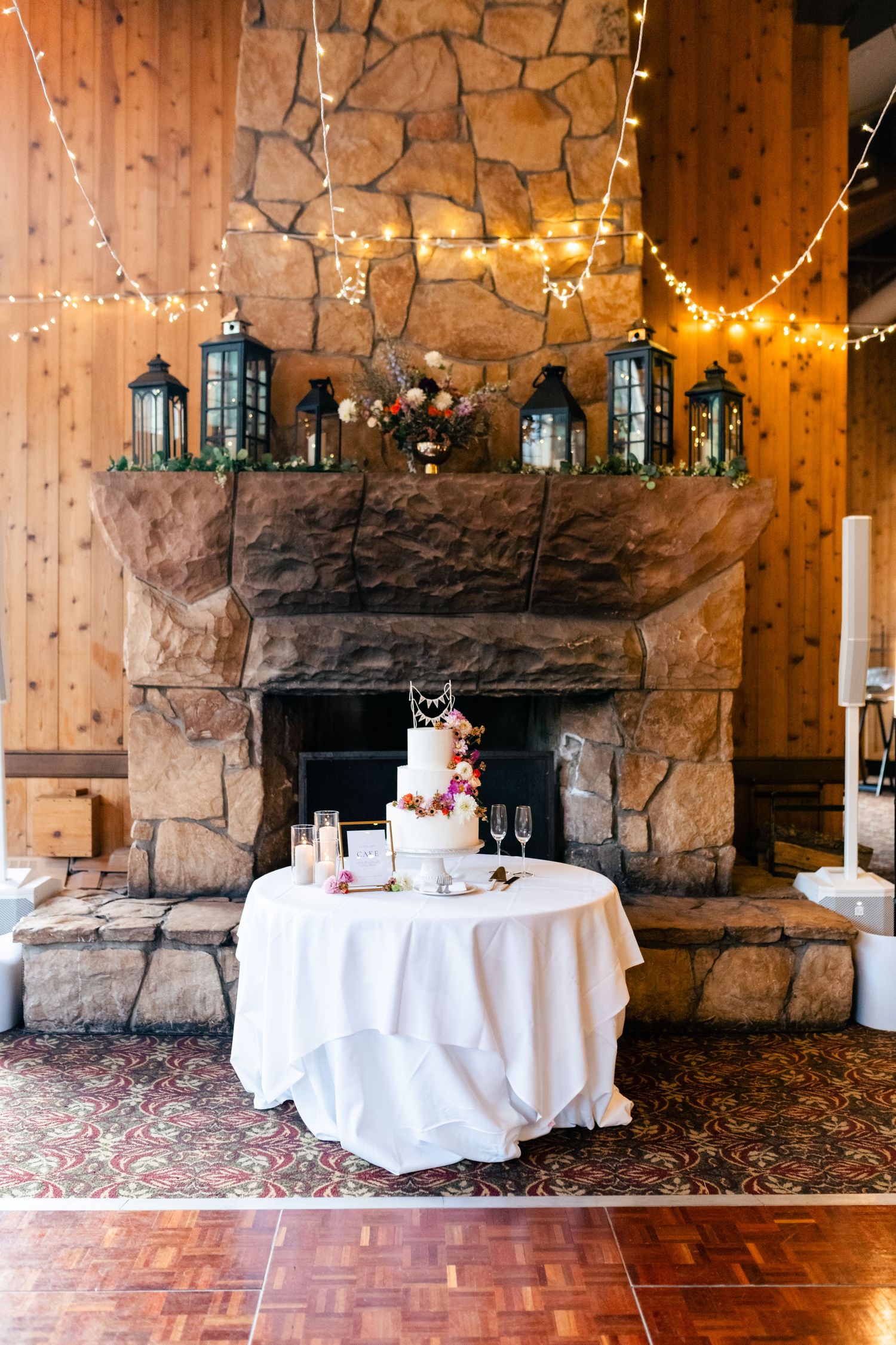 Wedding reception venue decorated with string lights and white tables against rustic stone walls and wooden beams.