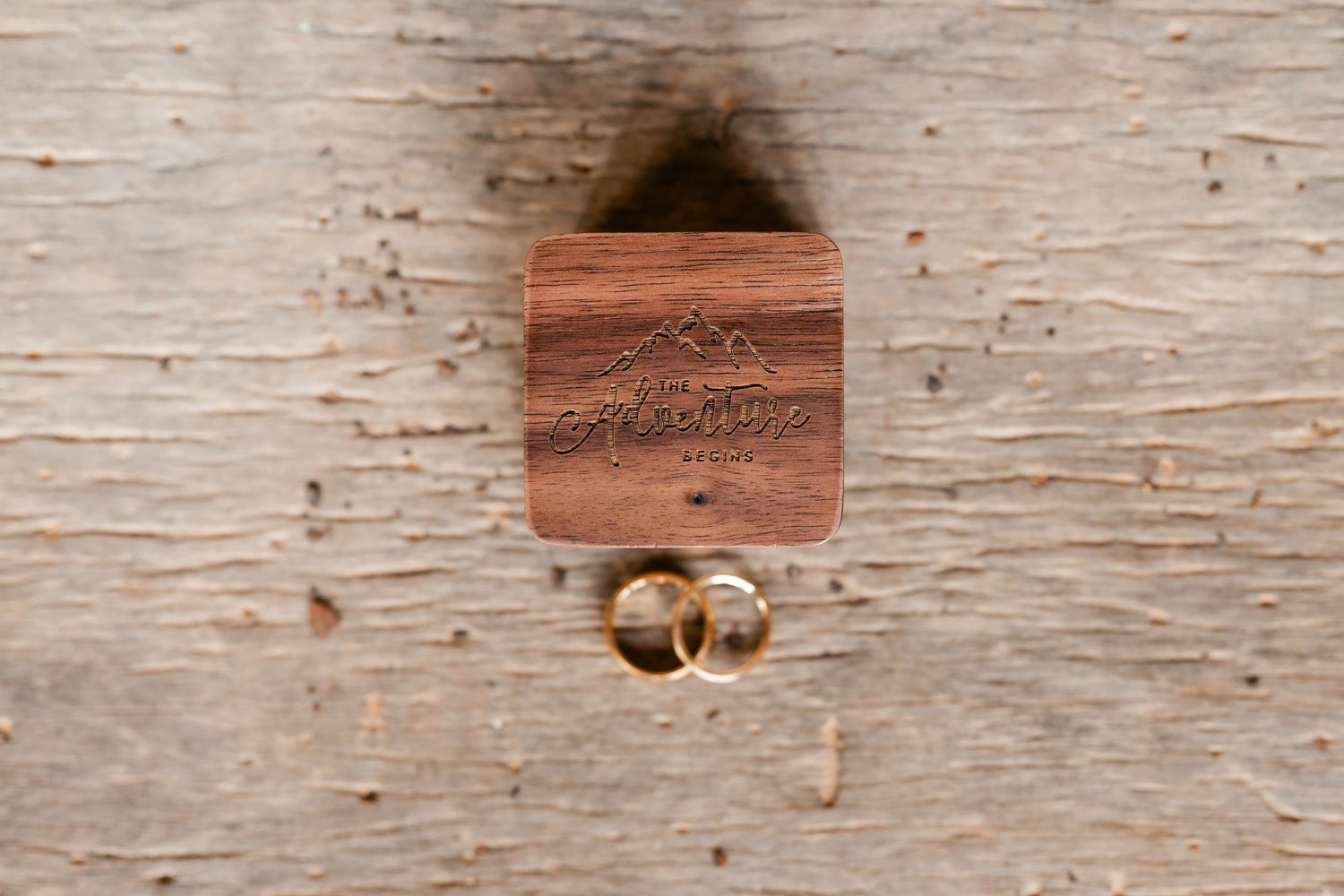 Wooden ring box with wedding bands on weathered wood surface.
