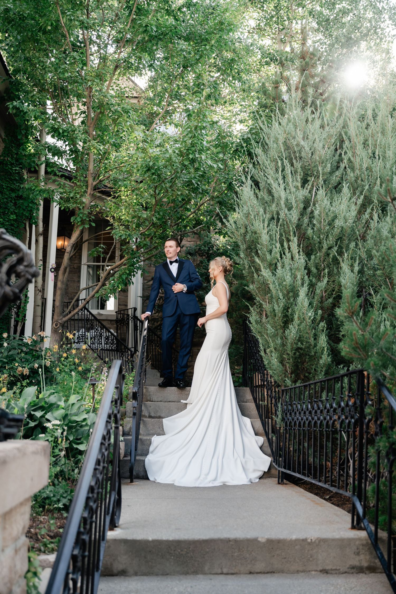 Wedding couple poses on outdoor garden staircase surrounded by lush greenery.
