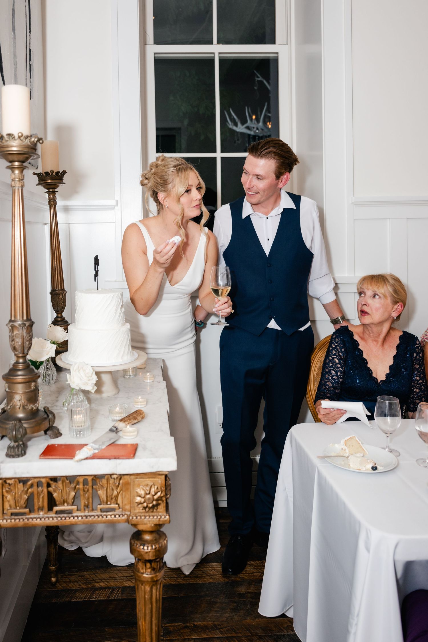 Wedding guests share laughter and conversation around elegant tables with white linens and ornate candelabras.
