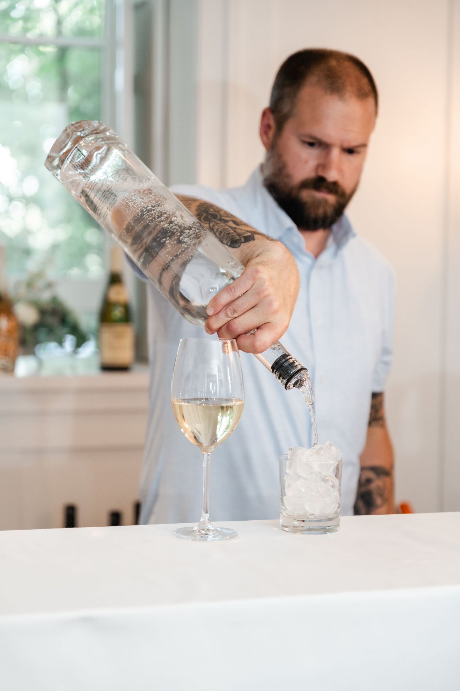 A bartender pours a white wine into a glass at an elegant table setting.