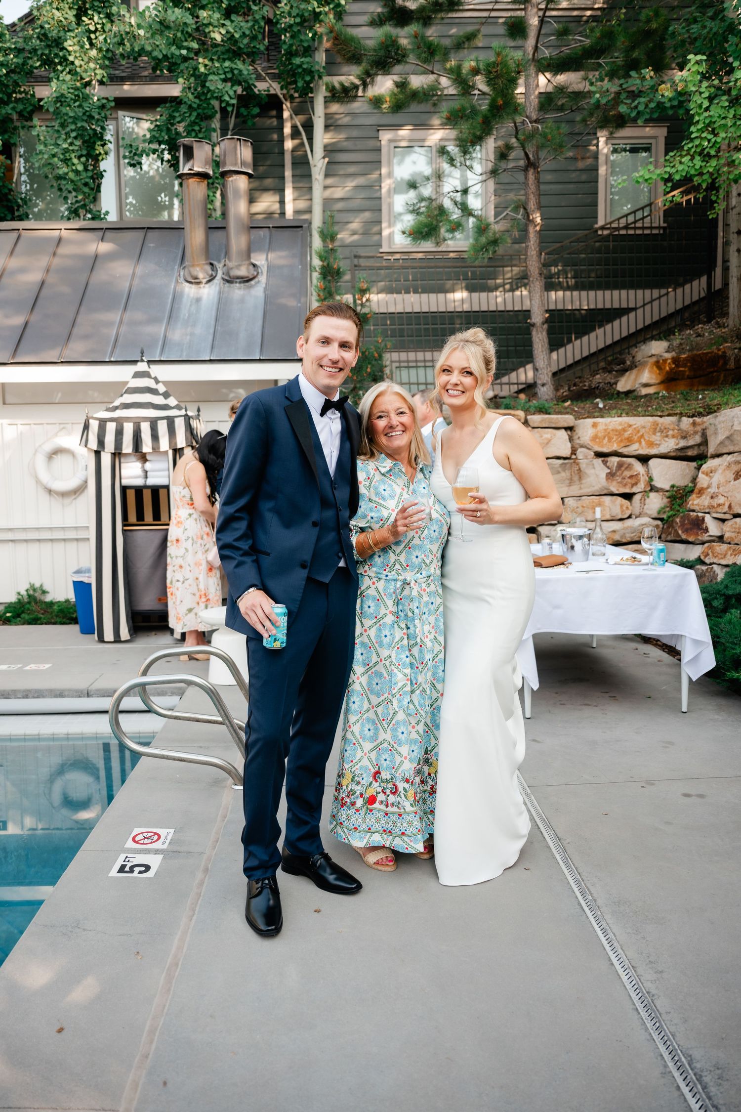 Outdoor wedding reception by pool with stone walls and trees creating natural ambiance.