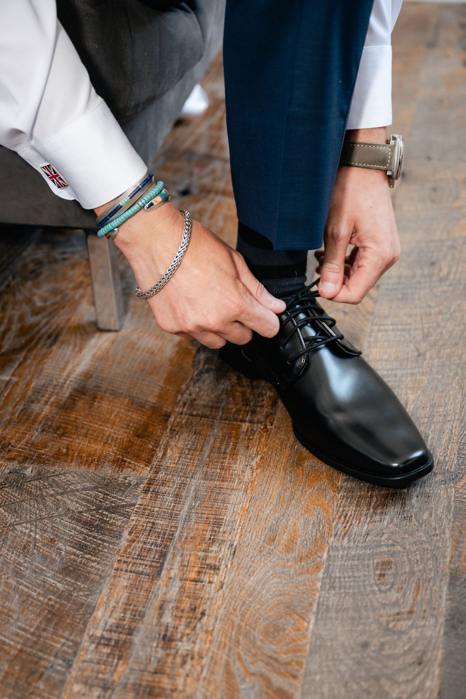 Detail shots of hands tying formal black dress shoes on wooden floor.