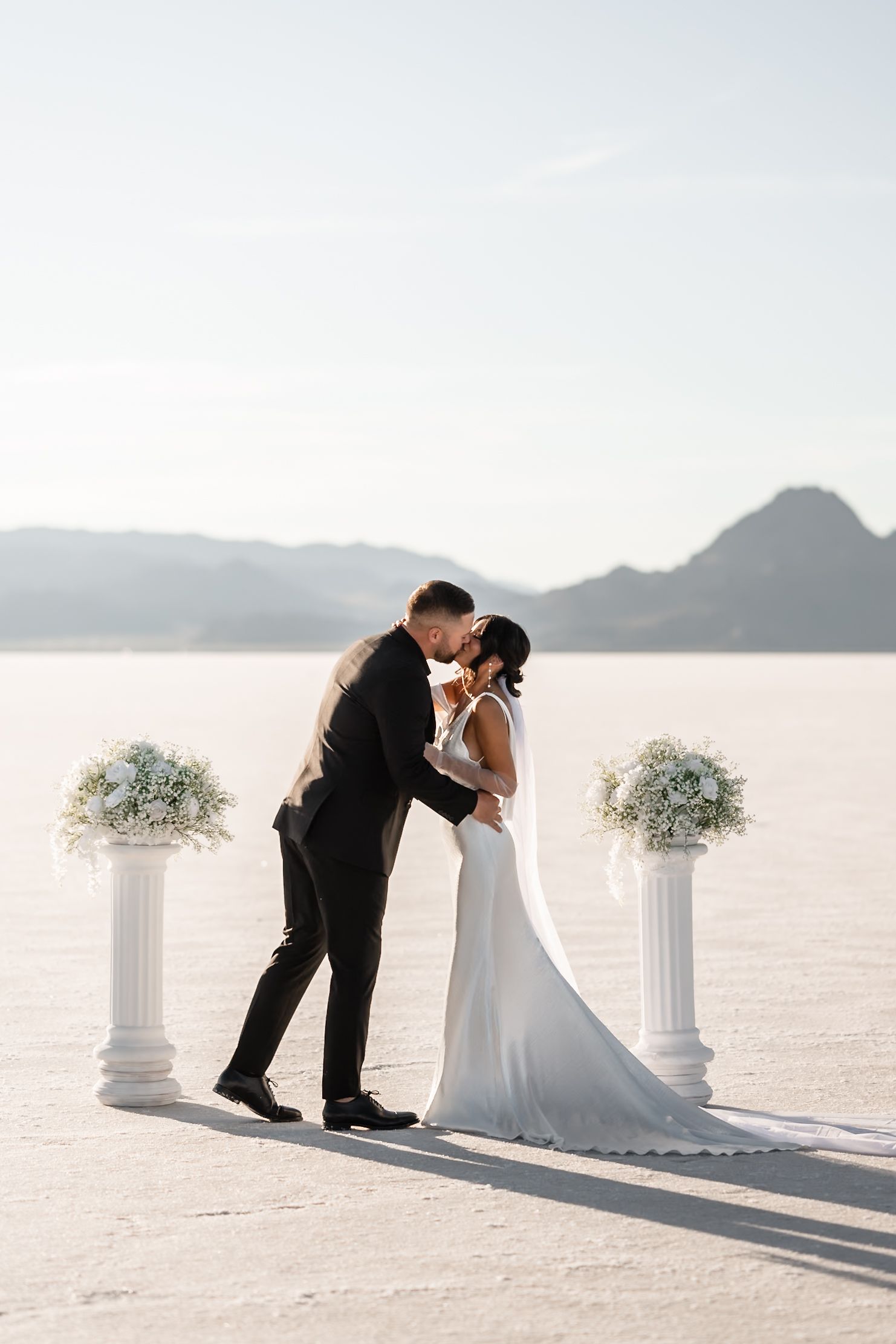 Romantic wedding ceremony moments captured on the Bonneville Salt Flats with white columns and mountains.