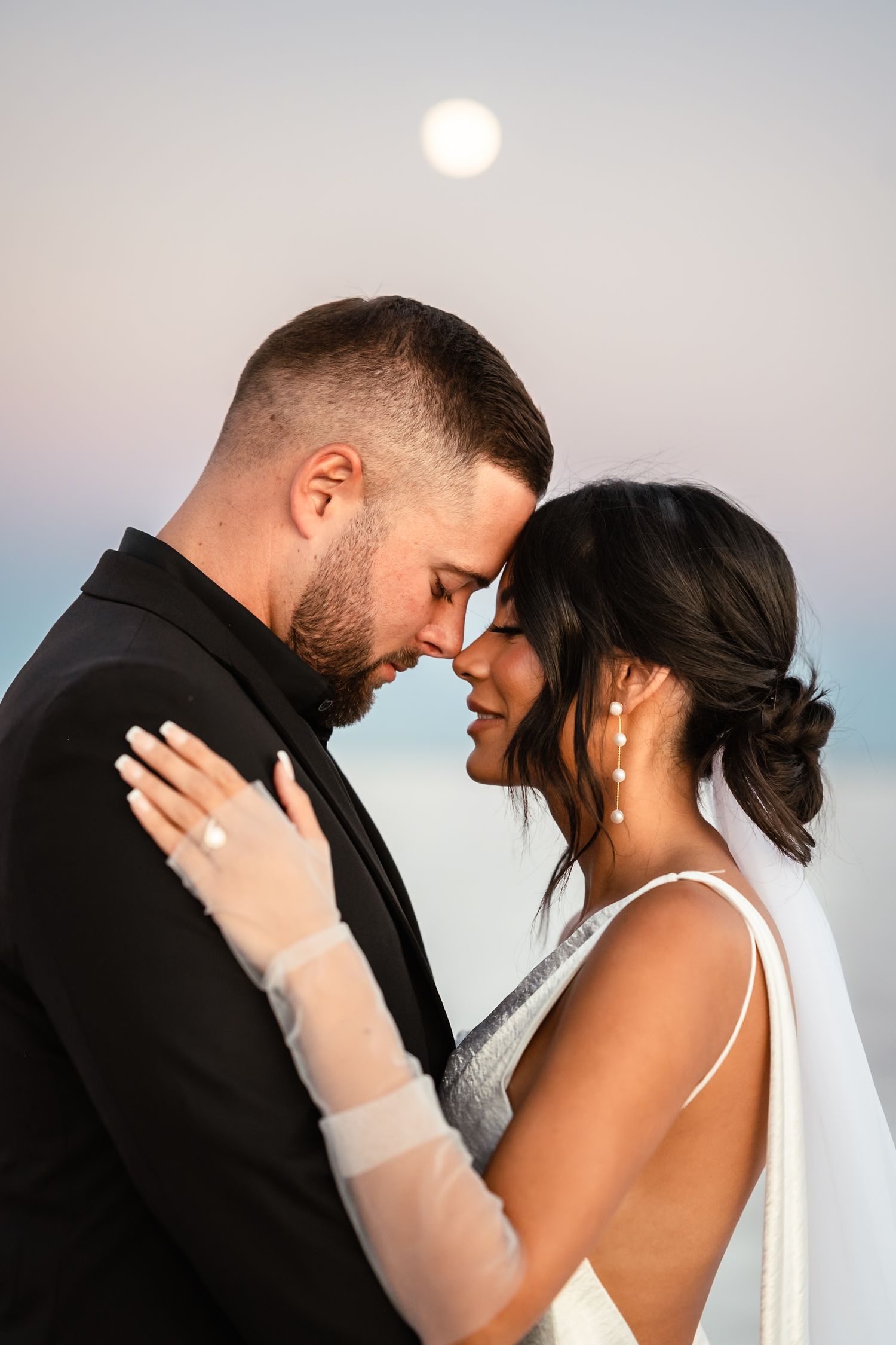 Romantic wedding couple embraces against sunset sky in intimate portrait series.