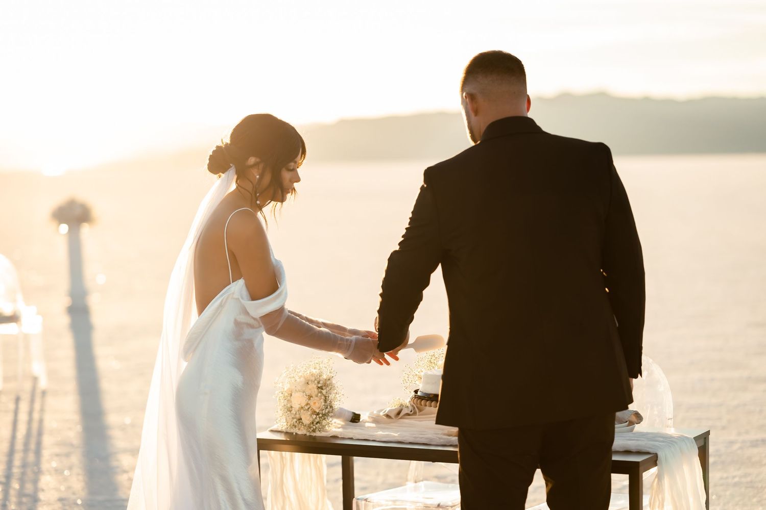 Silhouette of newlyweds against sunset sky on salt flats.