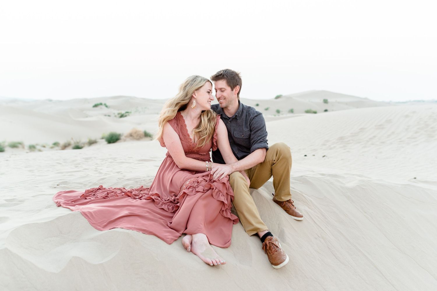 A romantic desert photoshoot with couple sitting together on sandy dunes.