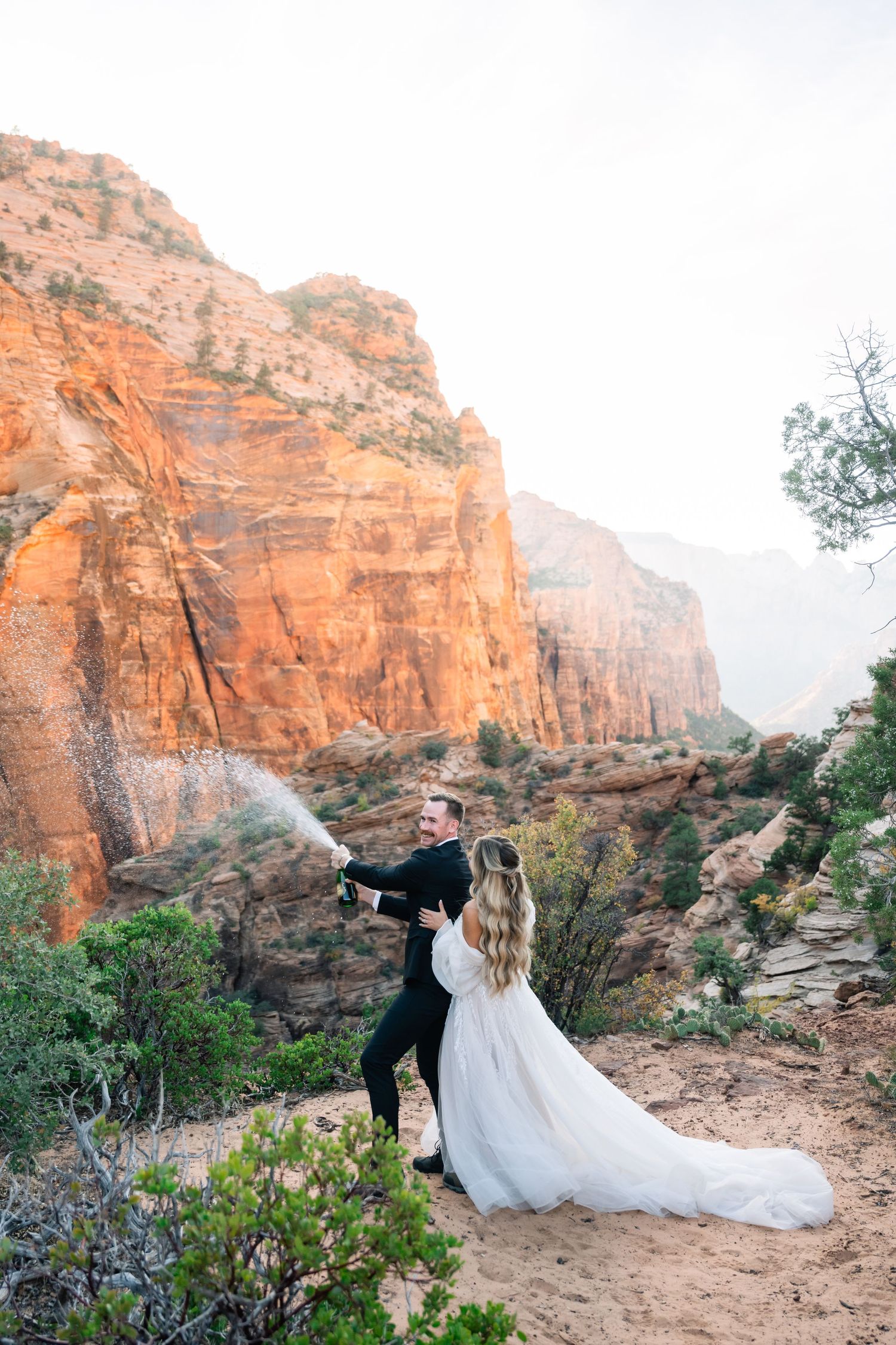 A couple embraces against stunning red rock cliffs during their wedding photoshoot.