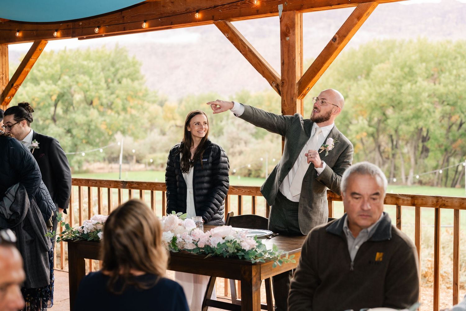 People gathered on a covered wooden deck overlooking a scenic mountain landscape.
