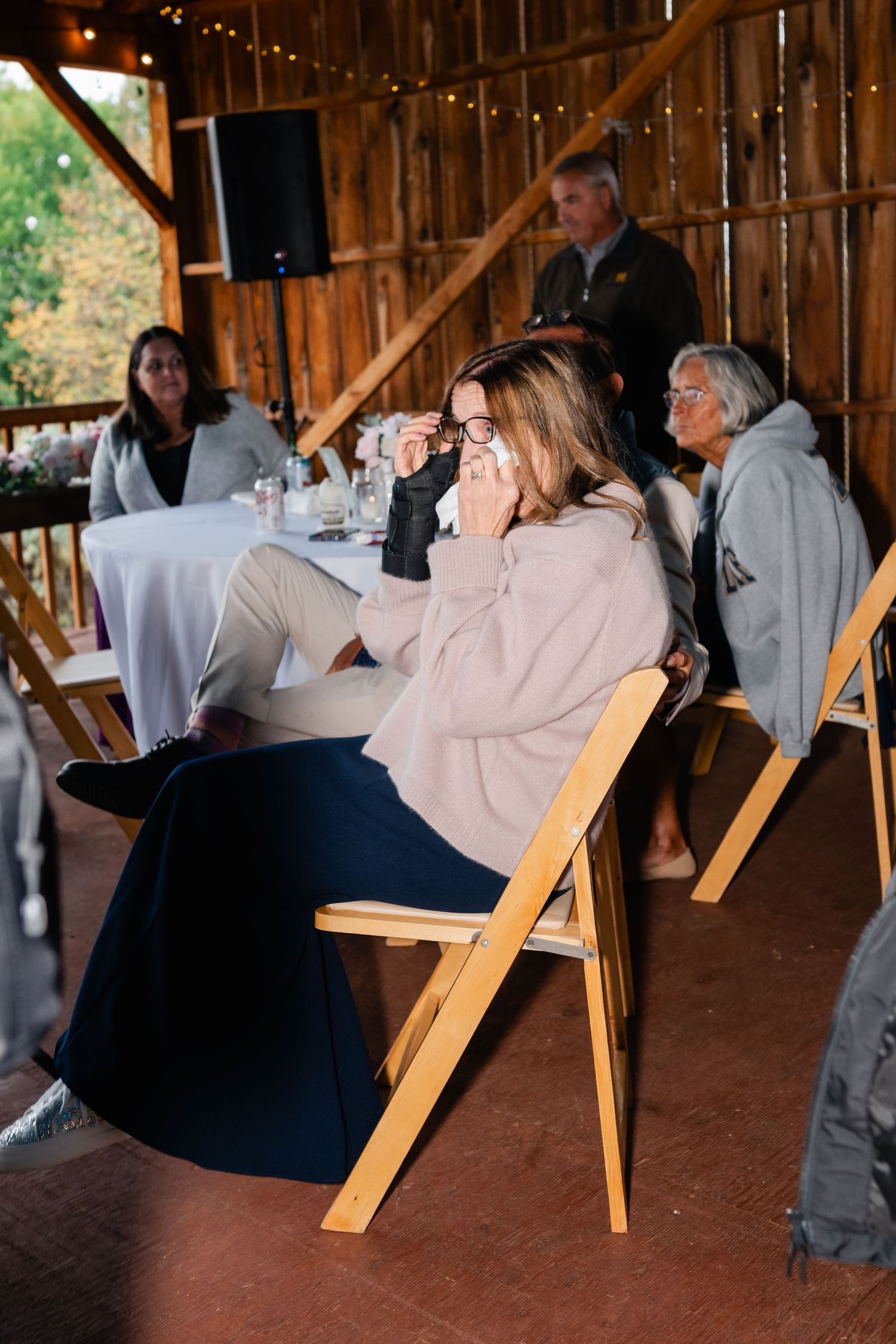 Wedding guests seated at tables in a rustic barn venue with string lights overhead.
