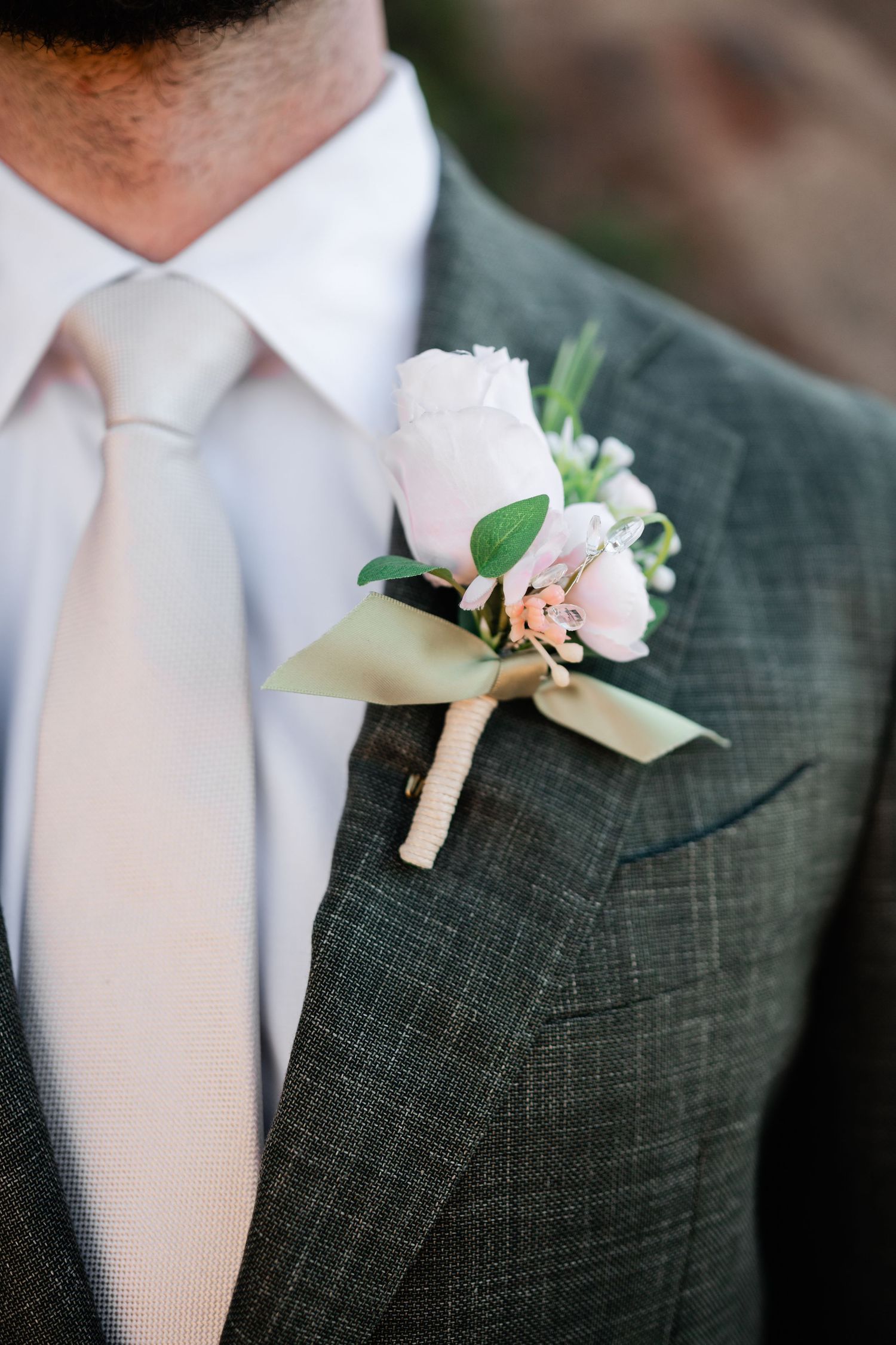 Close-up details of pink rose boutonnieres pinned to dark gray suit jackets with white dress shirts.