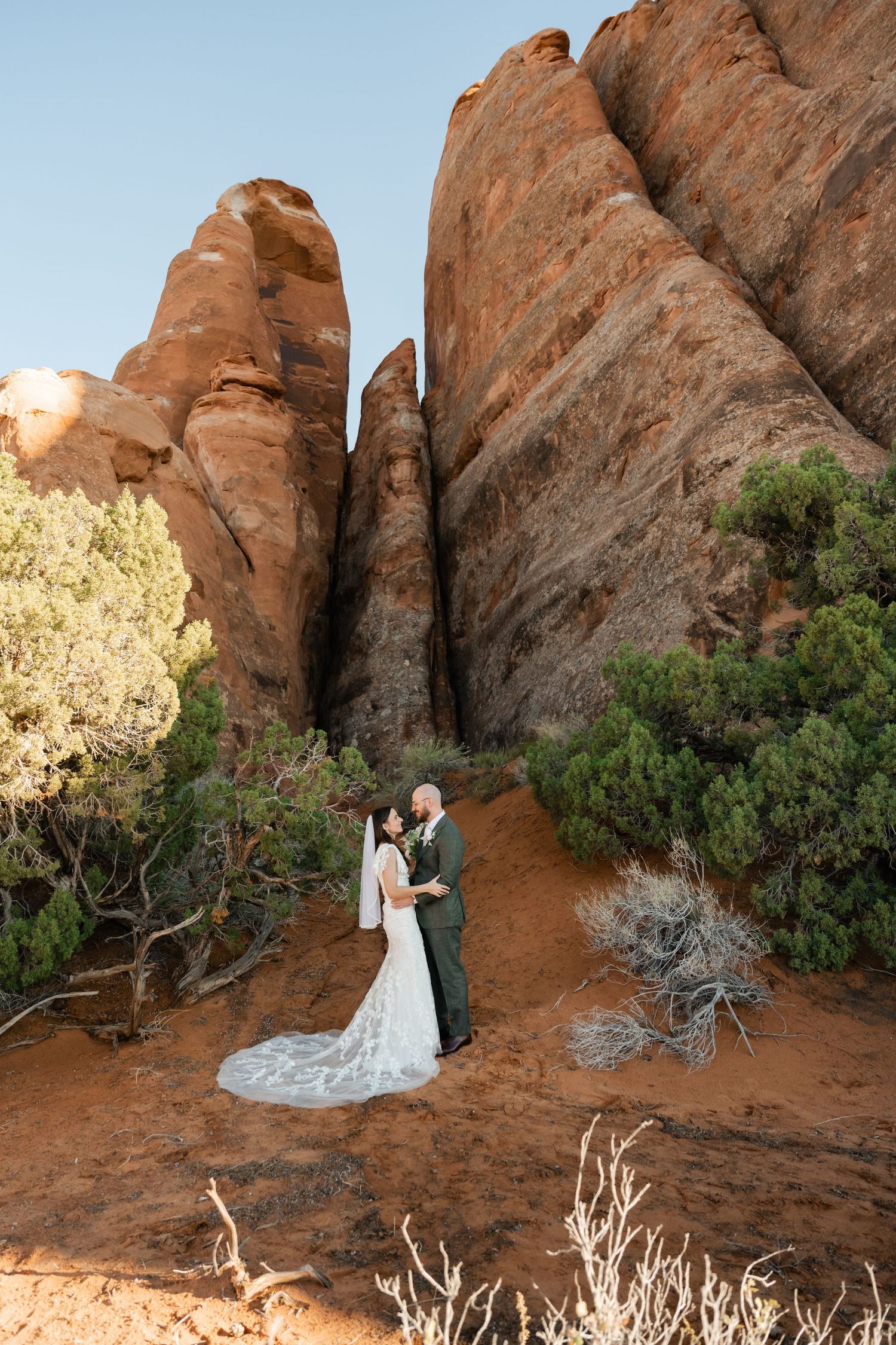 A couple poses for wedding photos against dramatic red rock formations in a desert landscape.