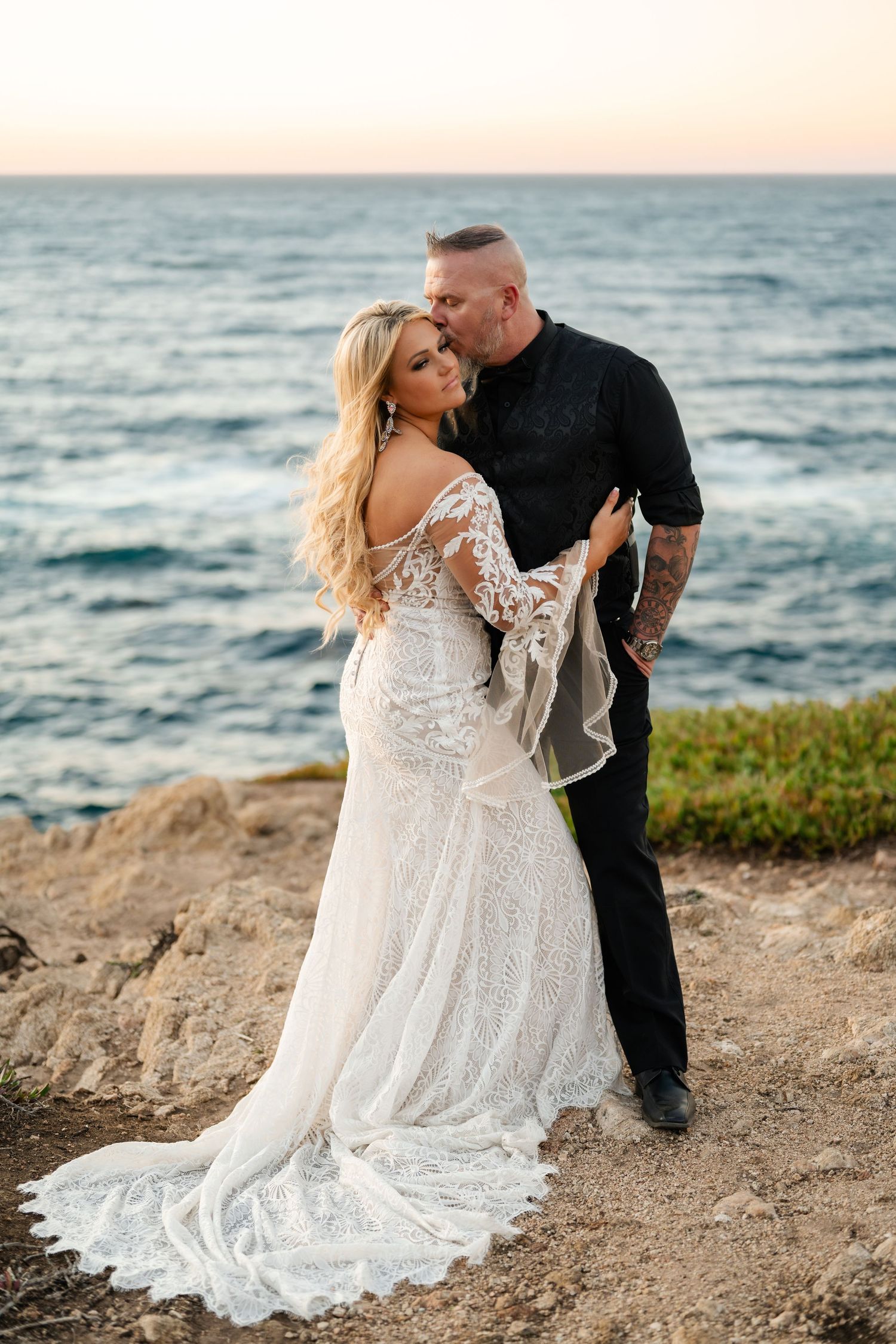 Romantic wedding photos on oceanside cliff with white lace dress and crashing waves.