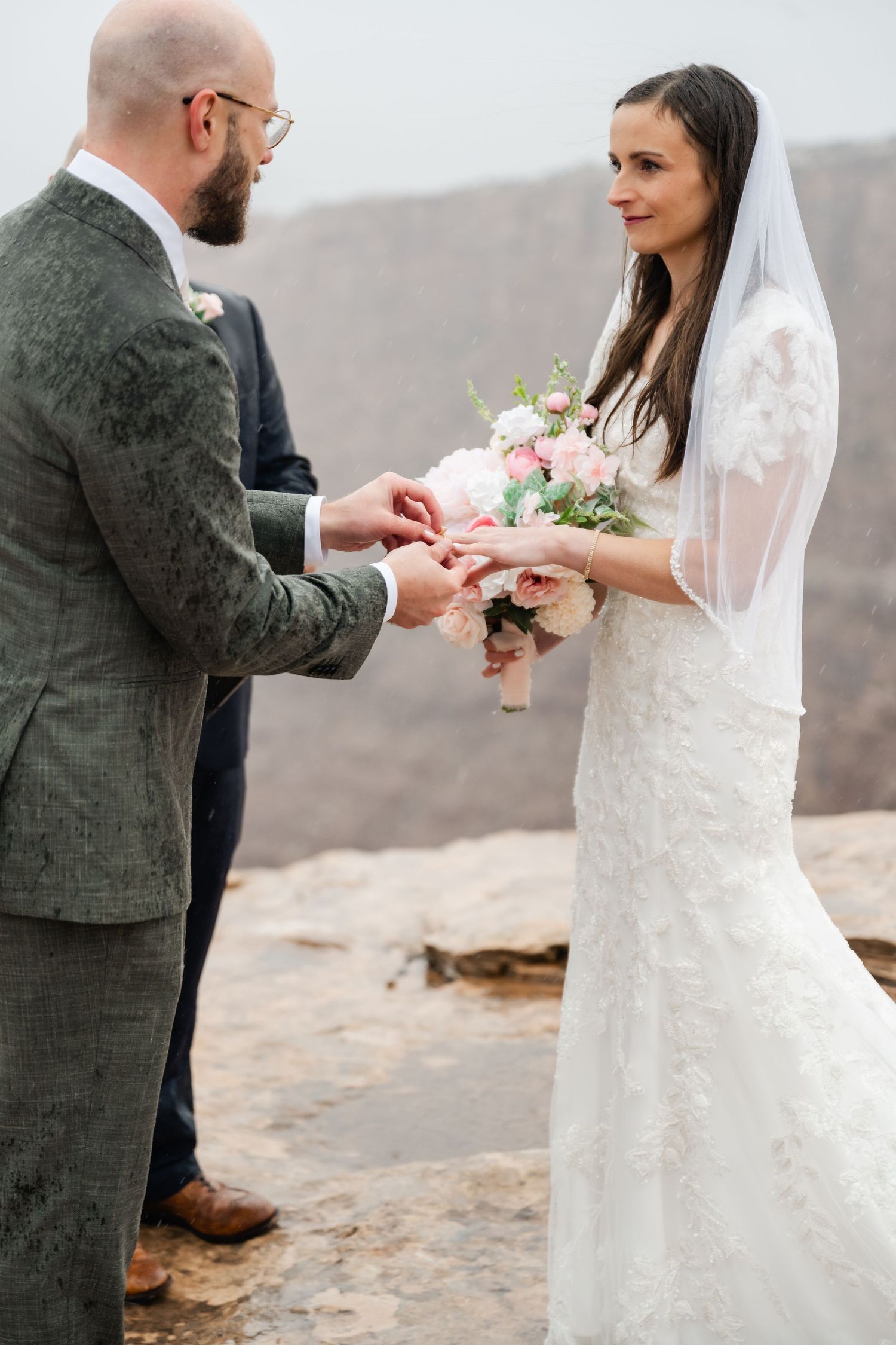 Wedding couple exchanging rings during intimate ceremony on desert cliff overlook.