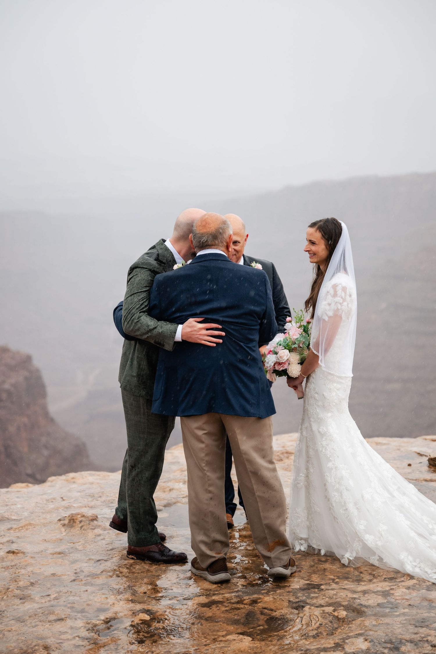 Emotional wedding moment captured on cliff edge with vast canyon landscape behind.