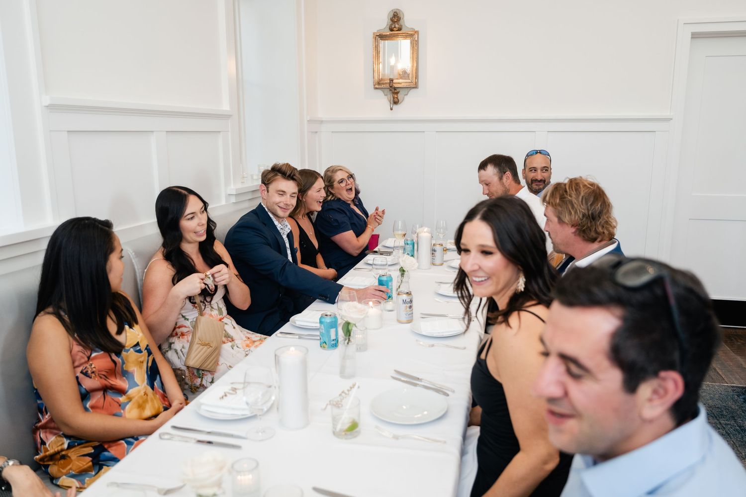 Guests gathered around a long dining table at an elegant indoor wedding reception, smiling and conversing.
