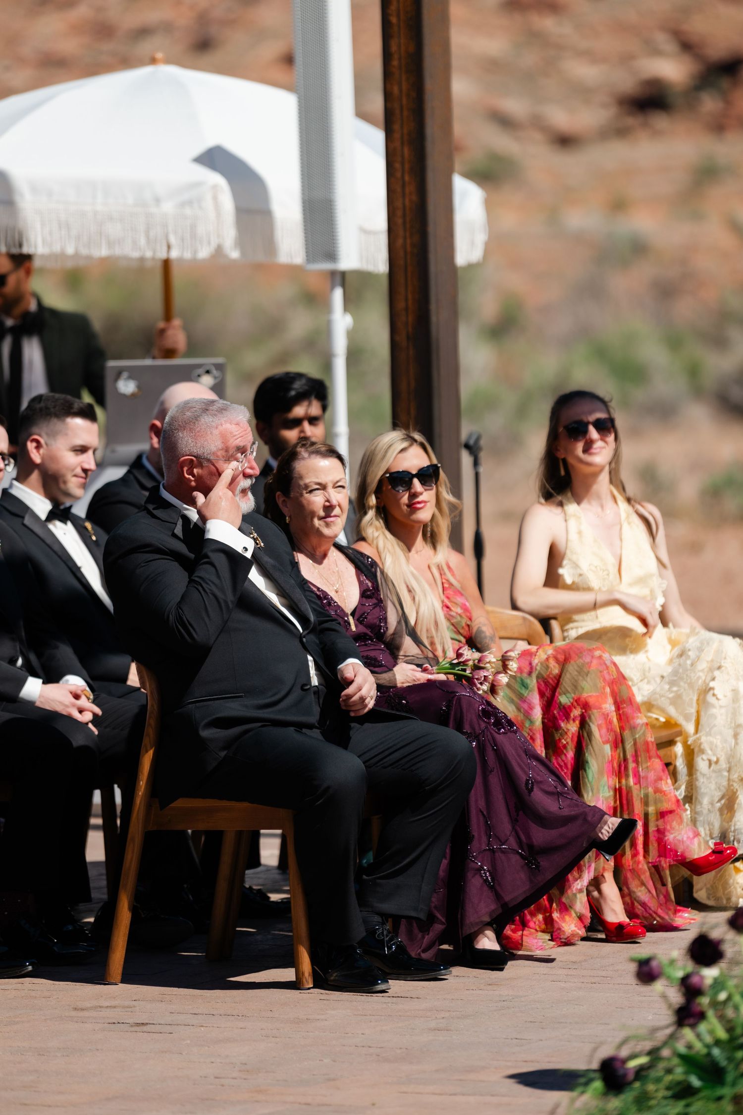 Guests seated outdoors at a wedding ceremony, smiling and emotional, with desert landscape in the background.