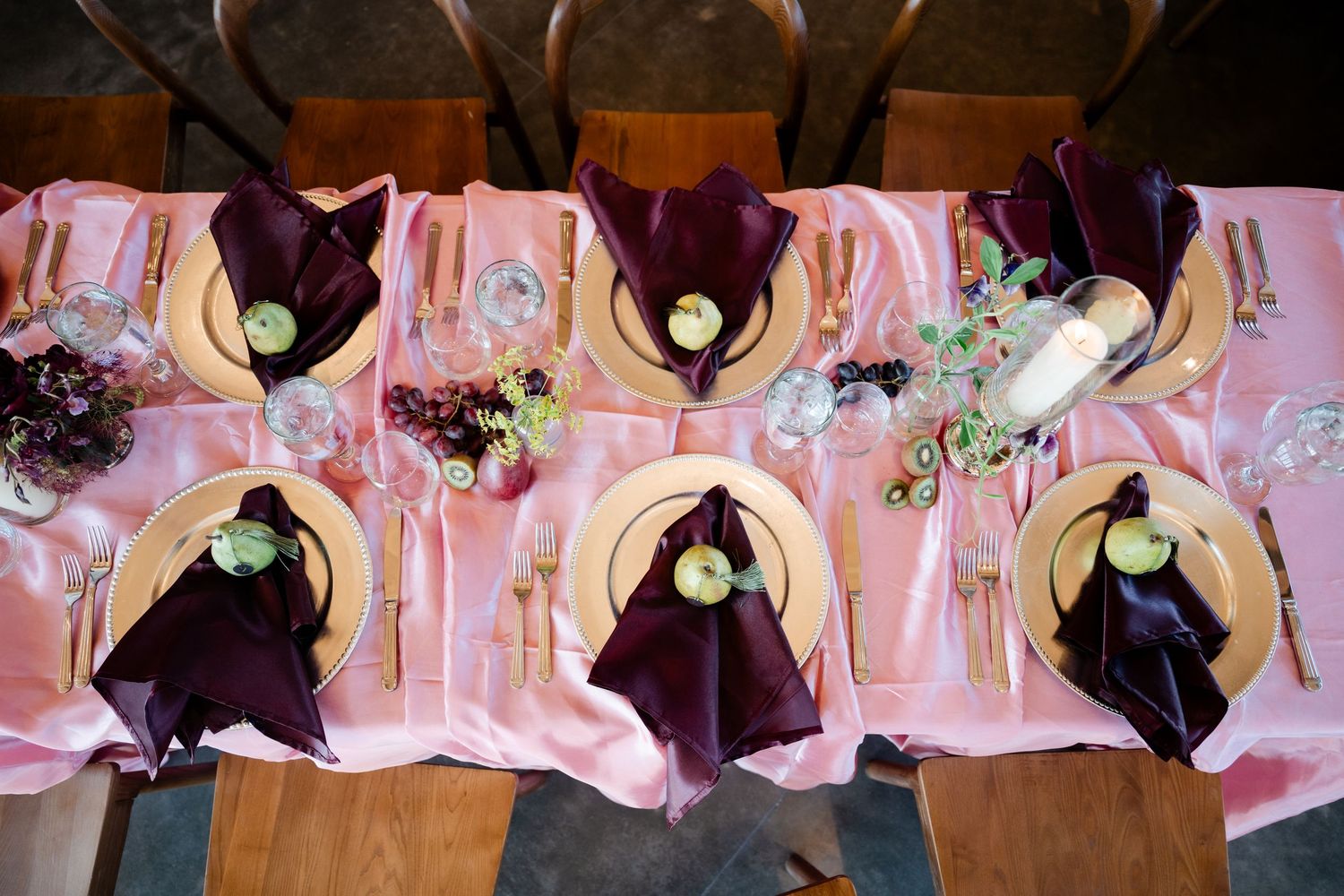 Aerial view of a pink satin wedding reception table with gold chargers, purple napkins, and green apple accents.