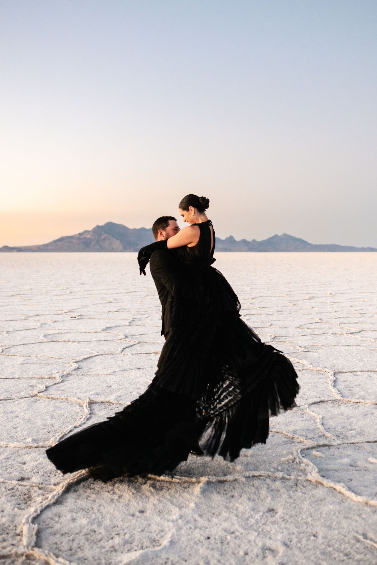 Utah Salt Flats Photographer. Romantic dance pose in black formal wear against sunset on salt flats.