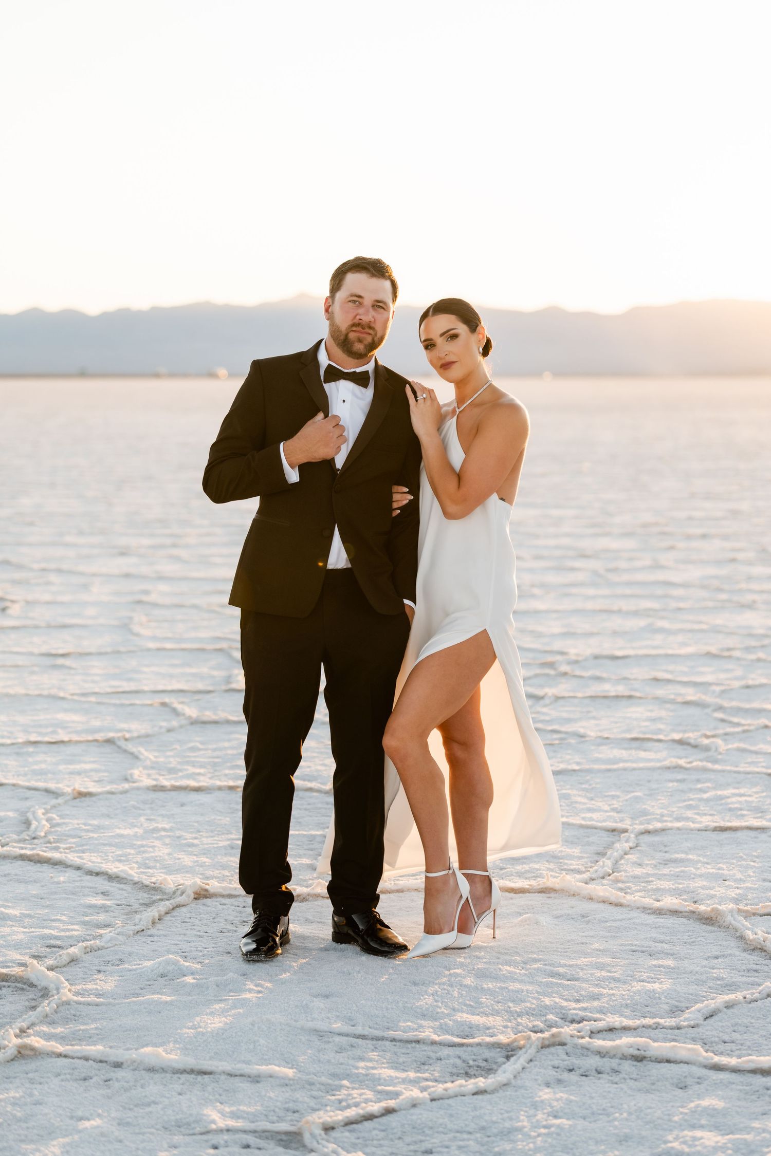 Utah Salt Flats Photographer. A couple poses playfully on the white salt flats wearing formal black and white attire.