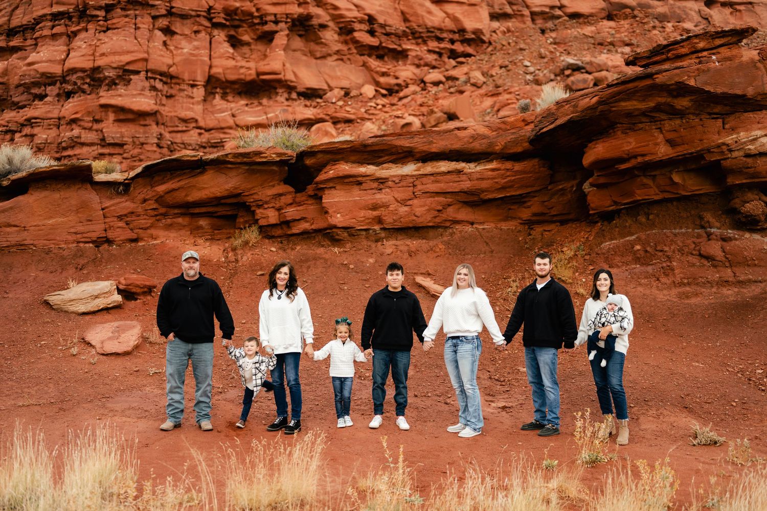 People stand in a row along a scenic red rock formation in a desert landscape at sunset.