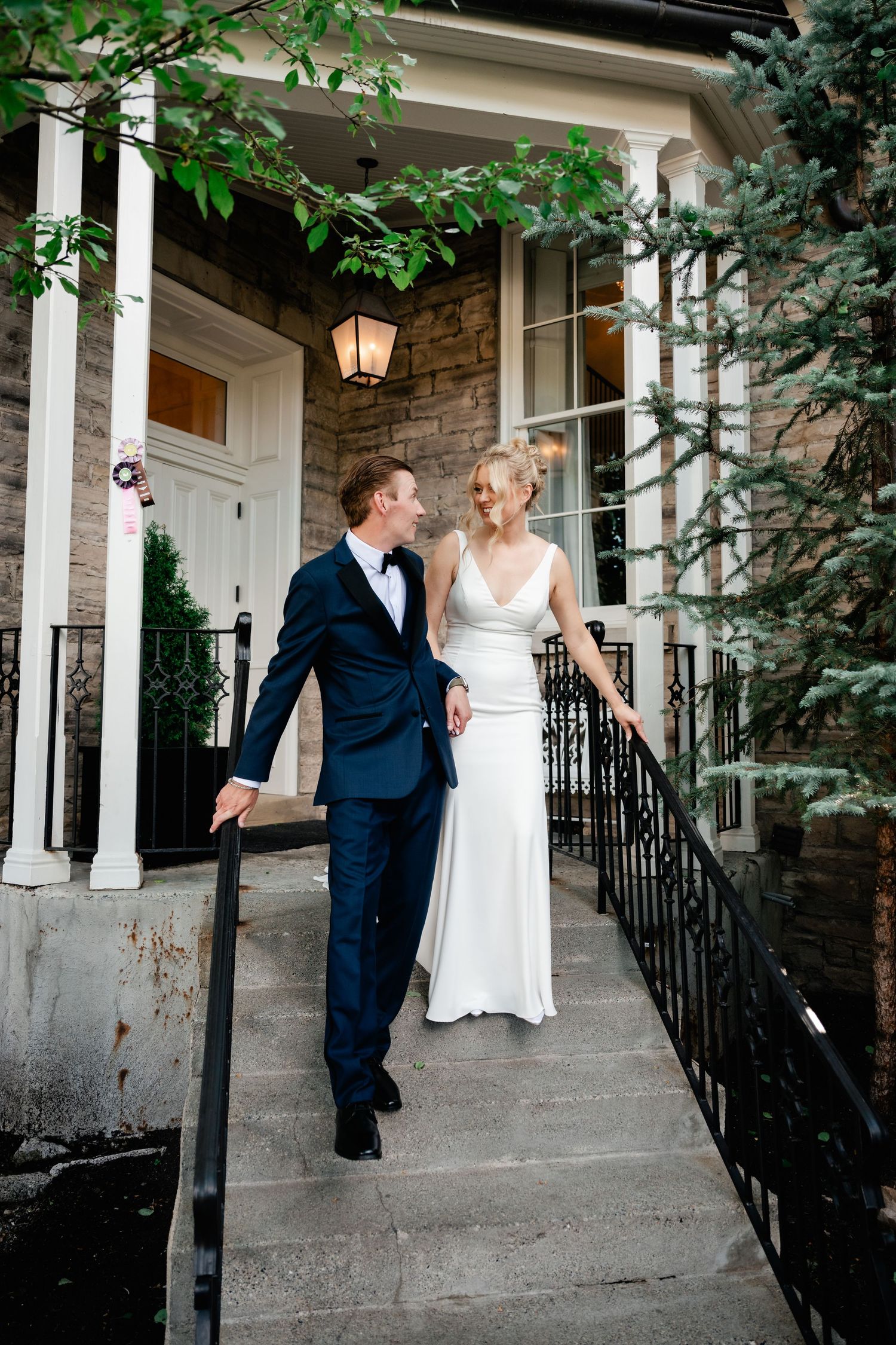 Bride and groom walk down stone steps outside the elegant Washington School House Hotel. she in white gown, he in navy tuxedo.