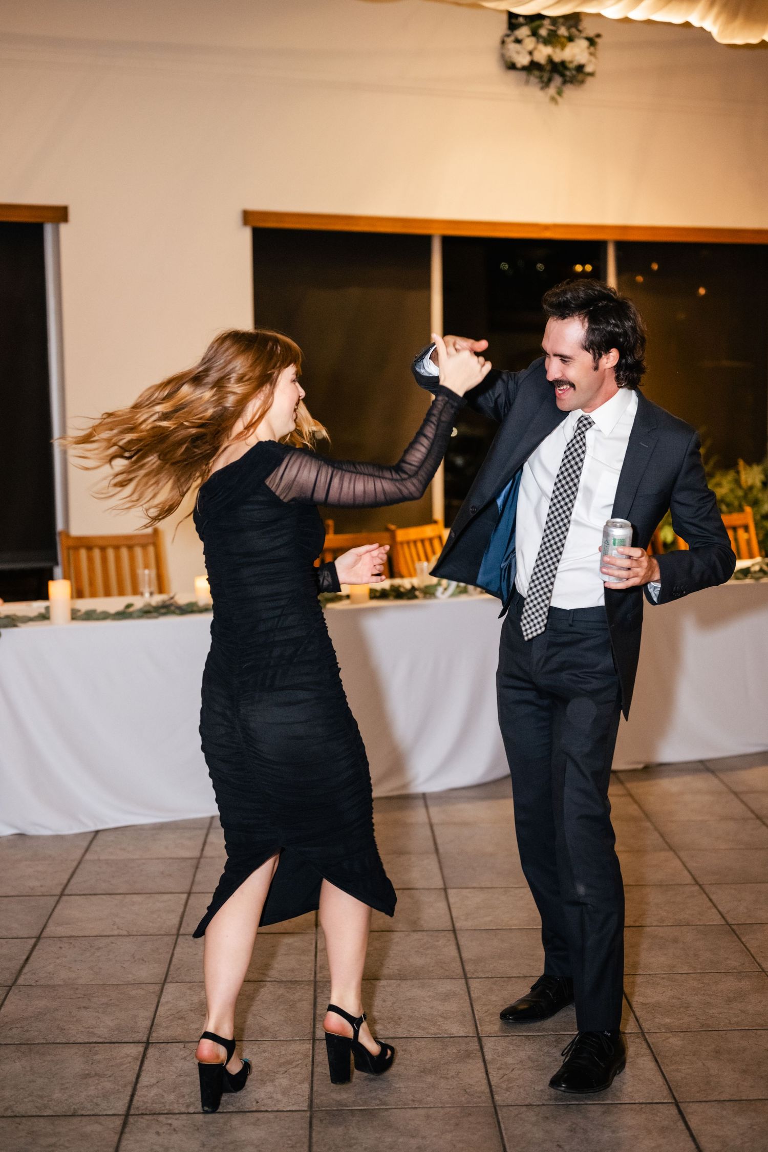 A couple dancing at a wedding reception, with the woman in a black dress spinning as her hair flows through the air.