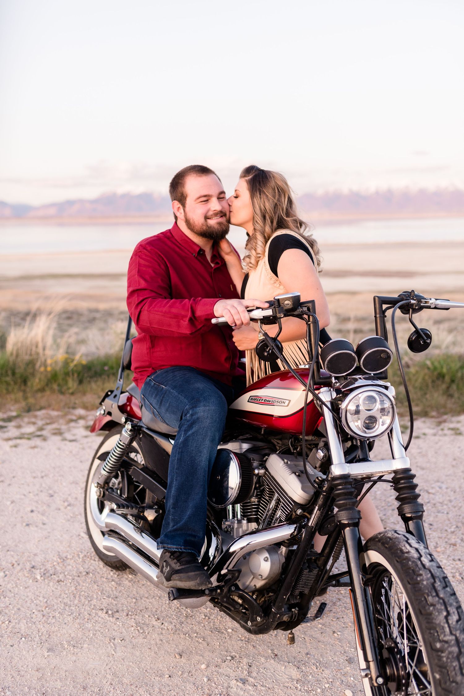 Couple sharing an intimate moment on a motorcycle against a desert mountain backdrop.