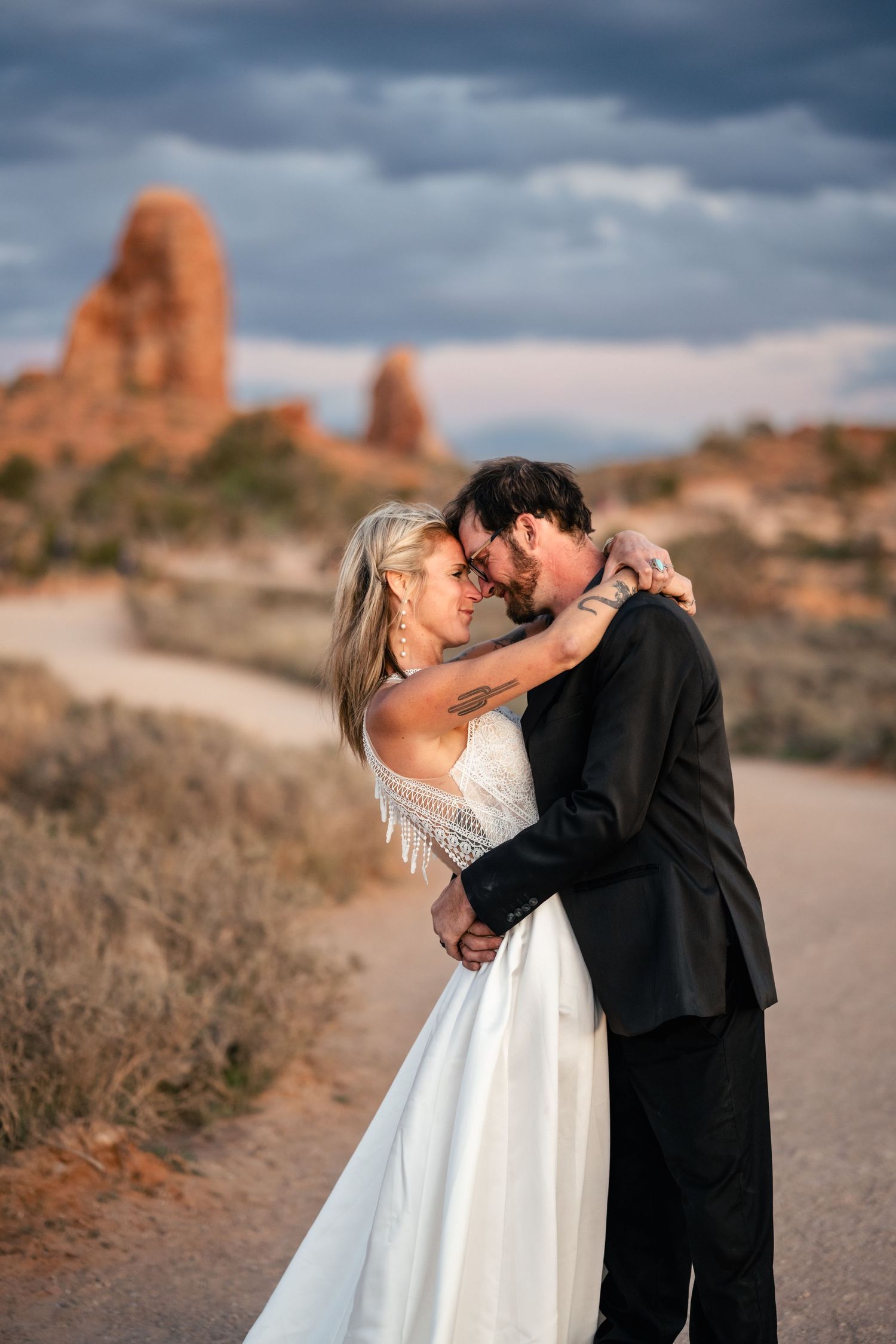 Wedding couple holds each other at the Windows in Arches NP on their elopement day by Utah Elopement Photographer