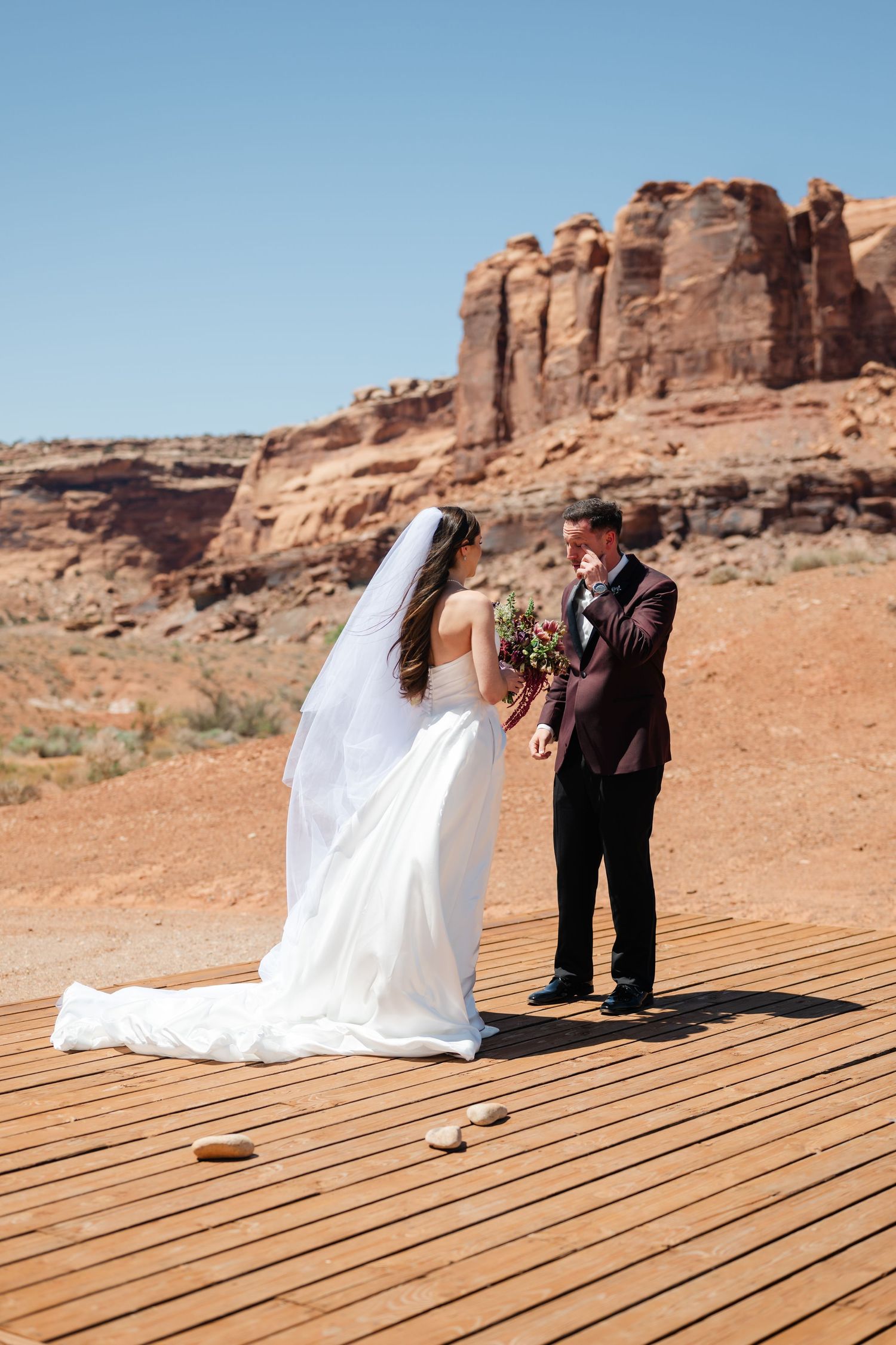 Bride and groom exchange vows on a wooden platform surrounded by red rock desert landscape at The Red Earth Venue in Moab, Utah.