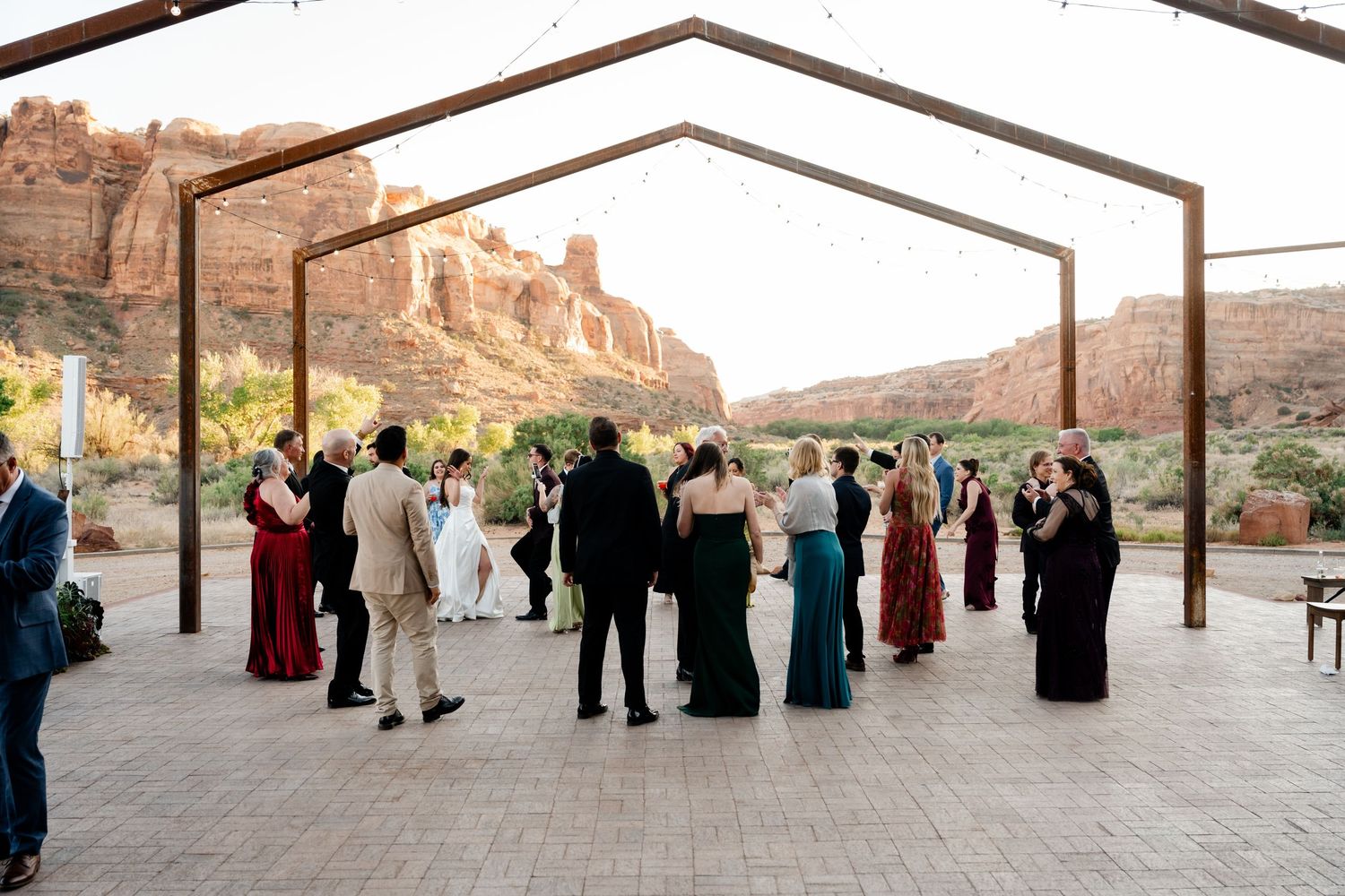 Outdoor wedding reception under rustic metal pergola with red rock canyon backdrop in desert landscape.