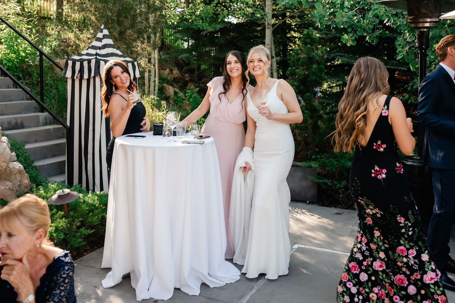 Wedding party members gather outdoors in formal attire and floral dresses.