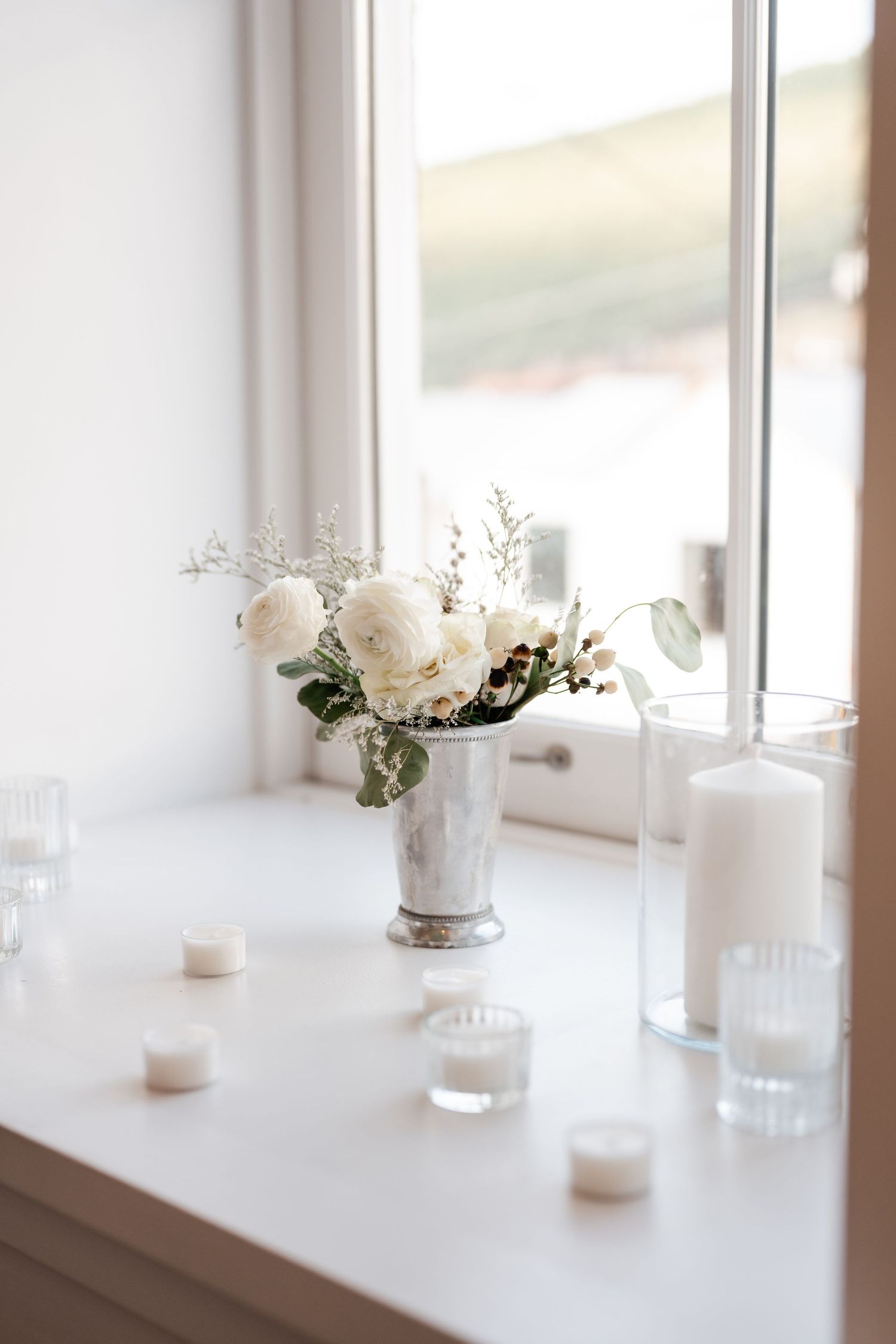 White floral arrangements and candles line a bright windowsill in an elegant setting.