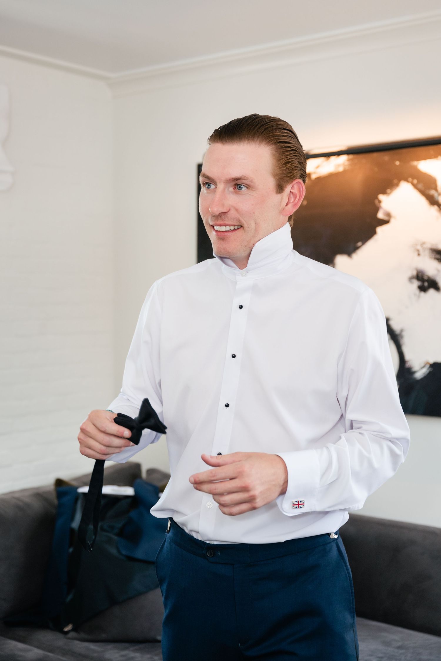 Someone in formal attire with a white dress shirt and navy pants adjusts their cuffs.