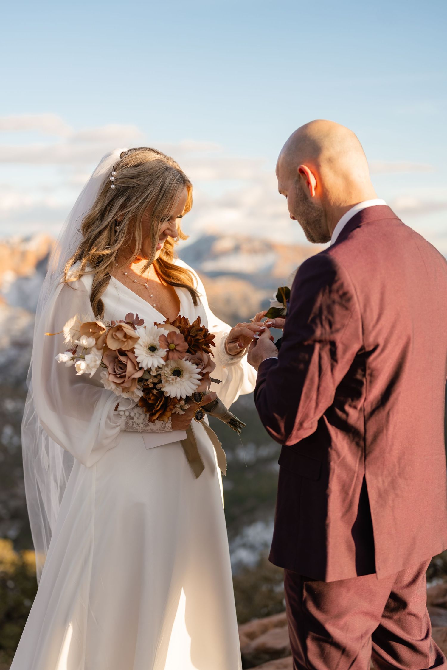 Wedding couple with white flowers against mountain backdrop during sunset.