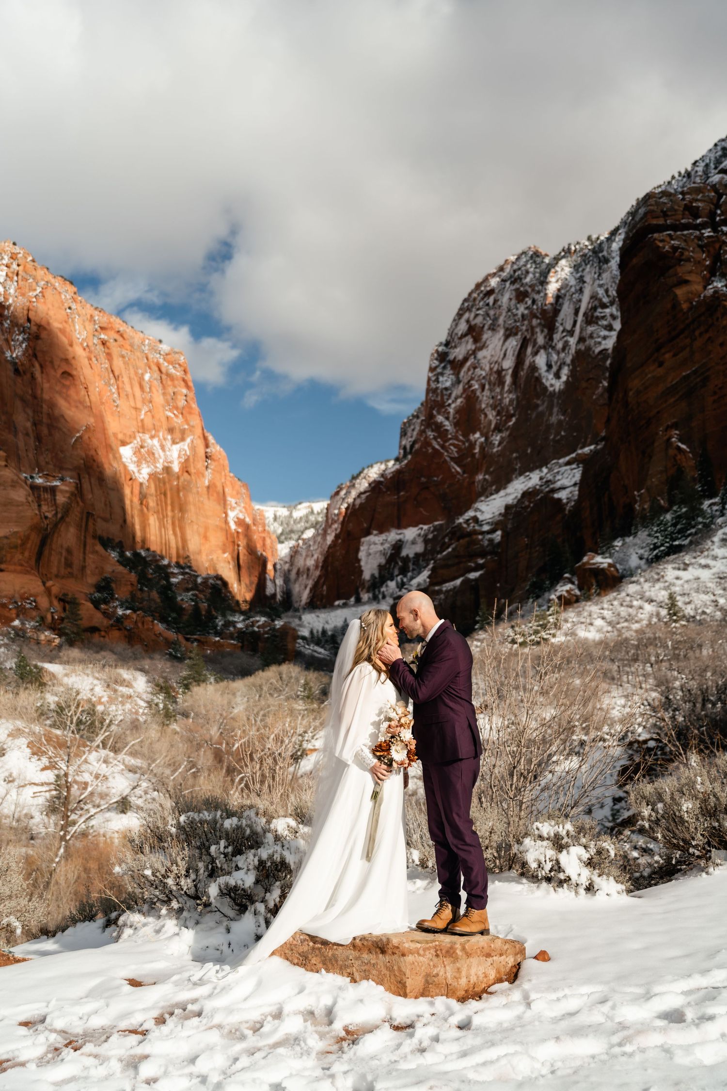 Couple embracing during their winter wedding with majestic red rock formations and snow in the background.