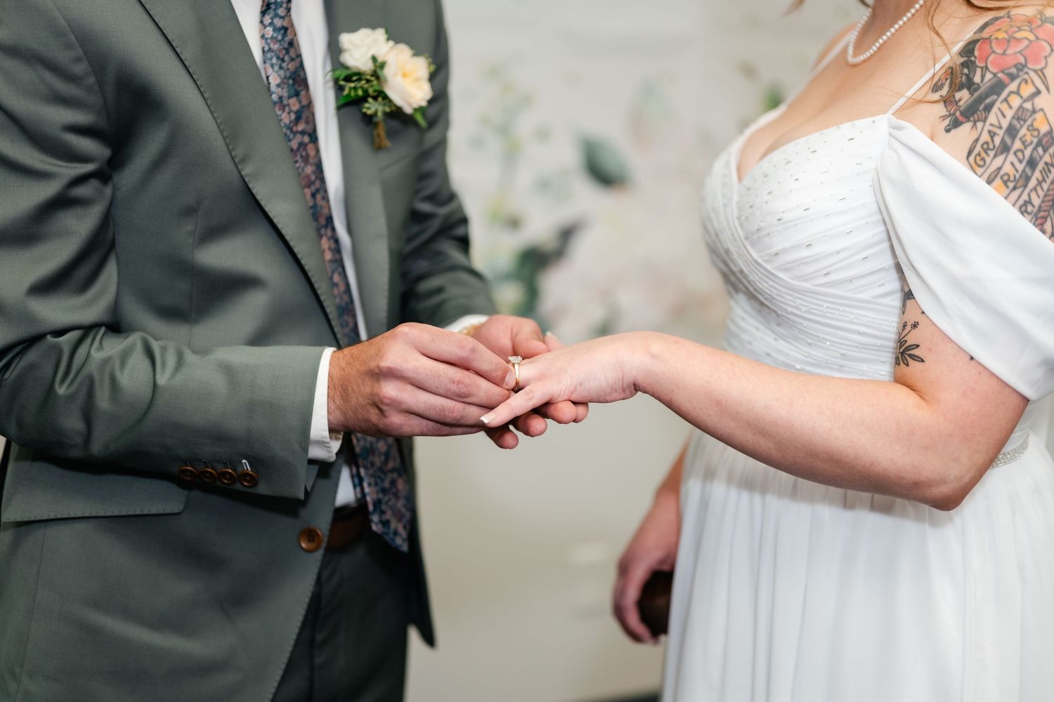 Close-up of hands exchanging rings during a wedding ceremony with a sage green suit visible.