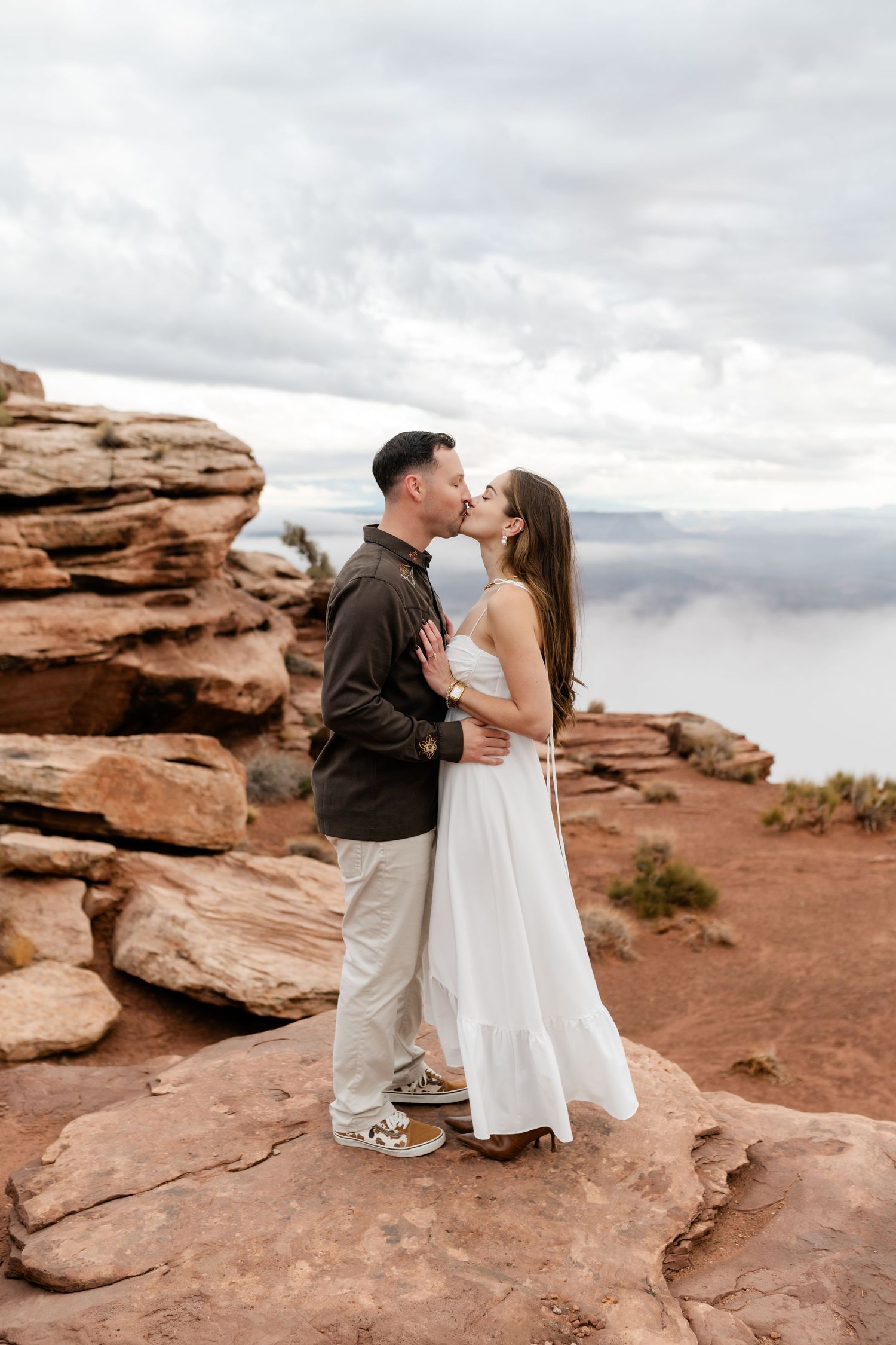 Romantic moment captured on red rock cliffs with cloudy sky and mountain views.