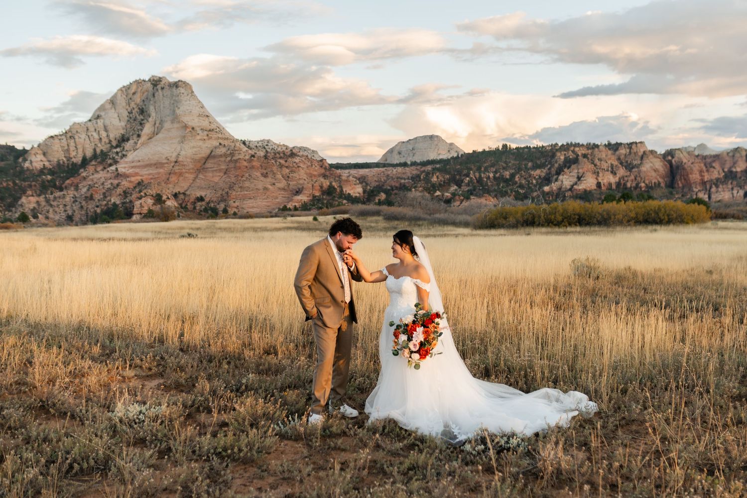 Rolling prairie field with dramatic mountain backdrop and glowing sunset sky.