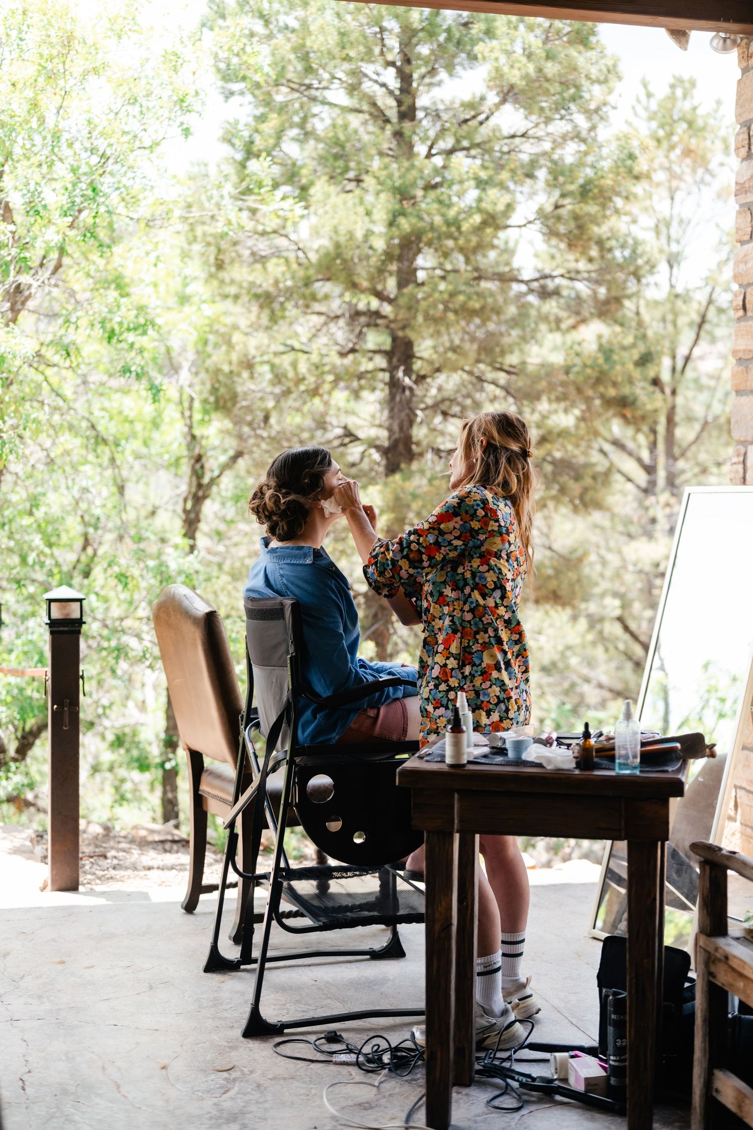 Outdoor covered patio workspace with people seated at desks surrounded by pine trees.