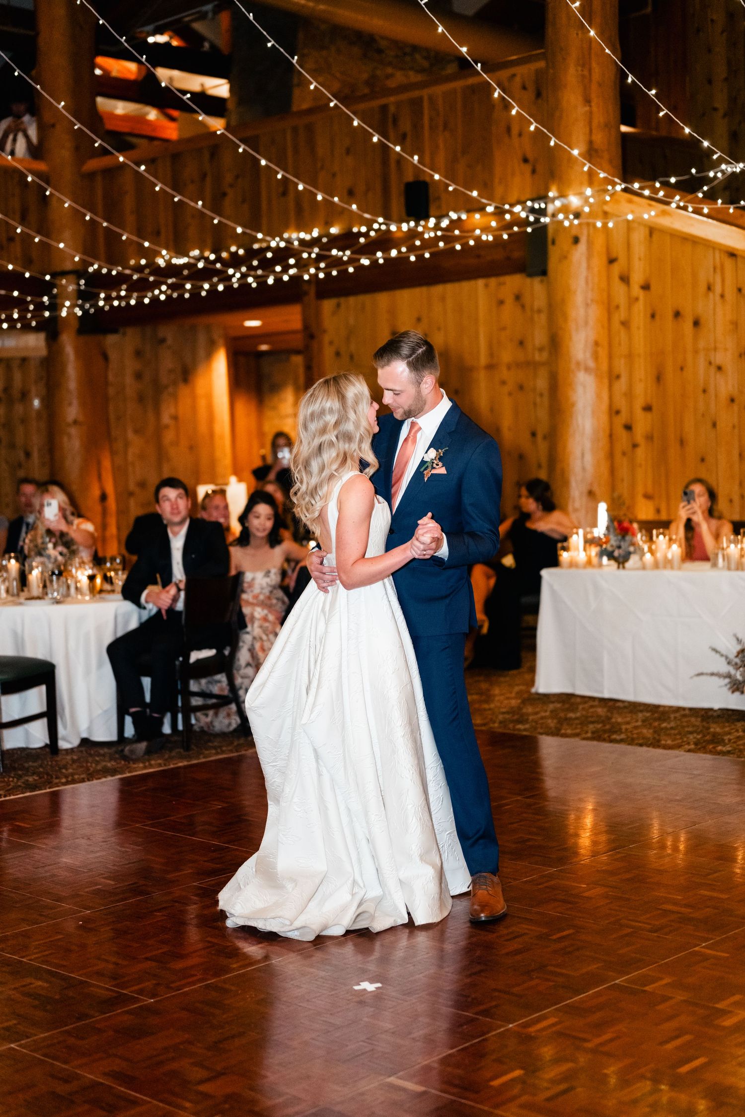 Couples dancing at rustic barn wedding reception under twinkling string lights.