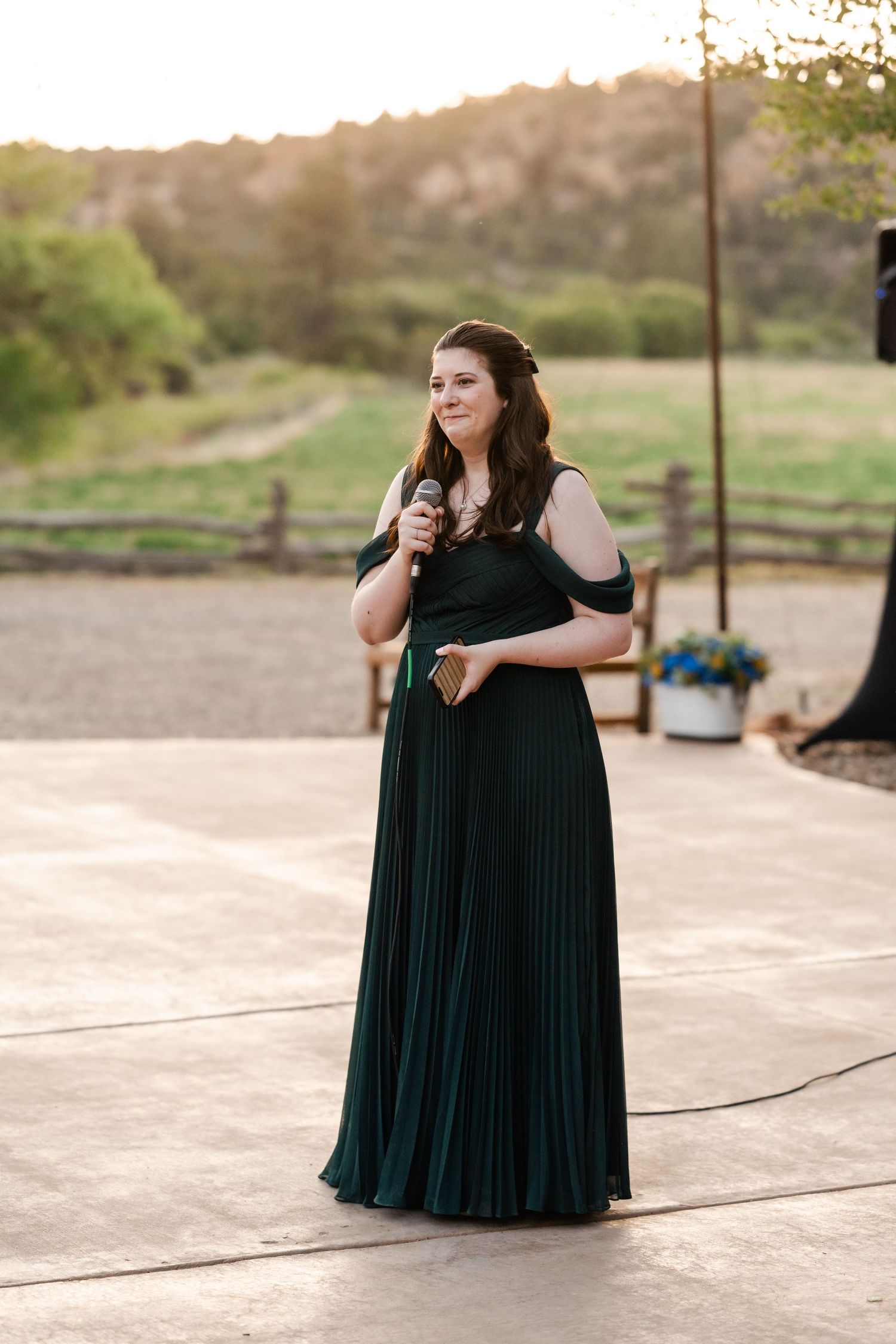 A person in a dark green formal dress stands outdoors at sunset.