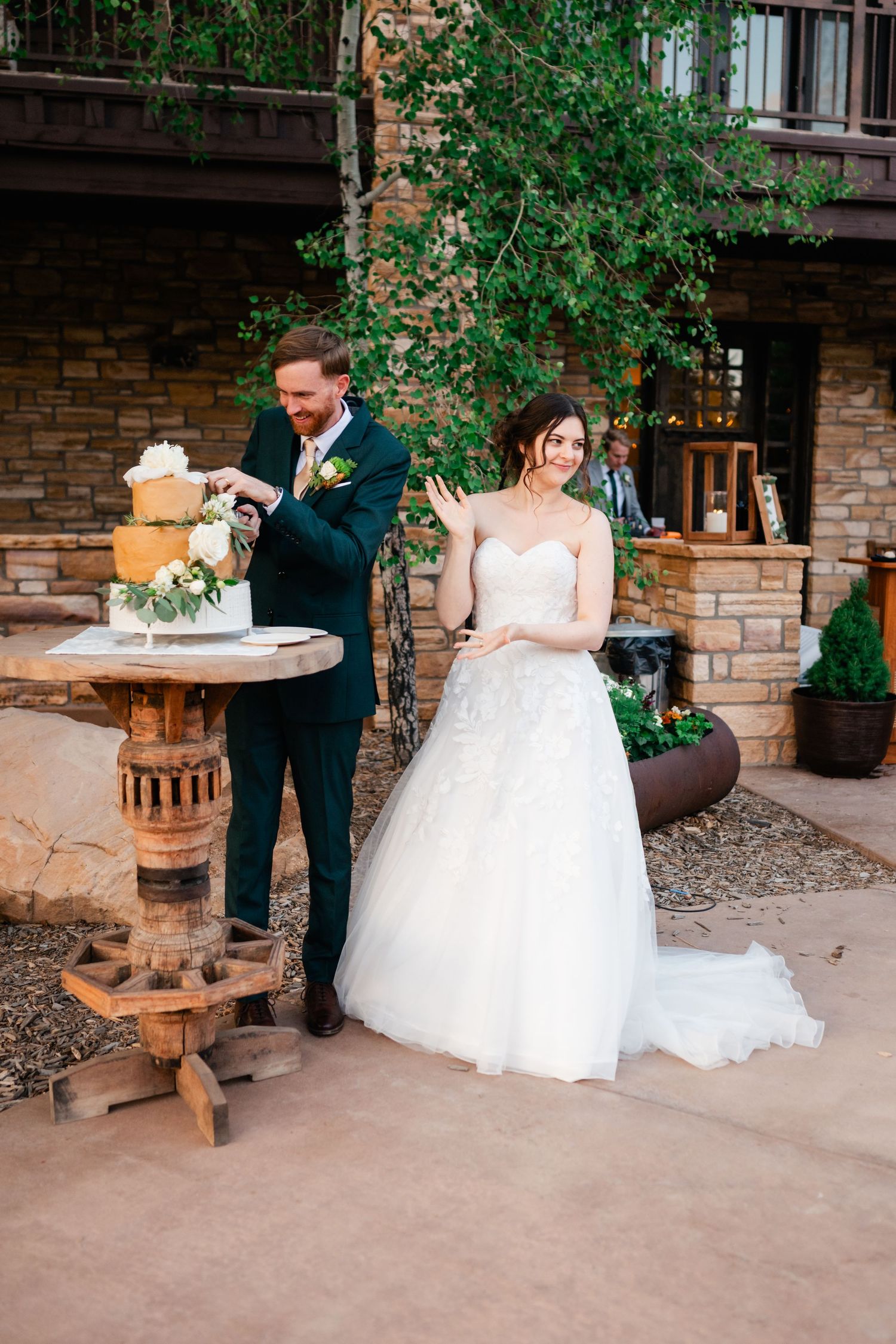 Couple cuts their wedding cake together at a rustic outdoor venue with stone walls.