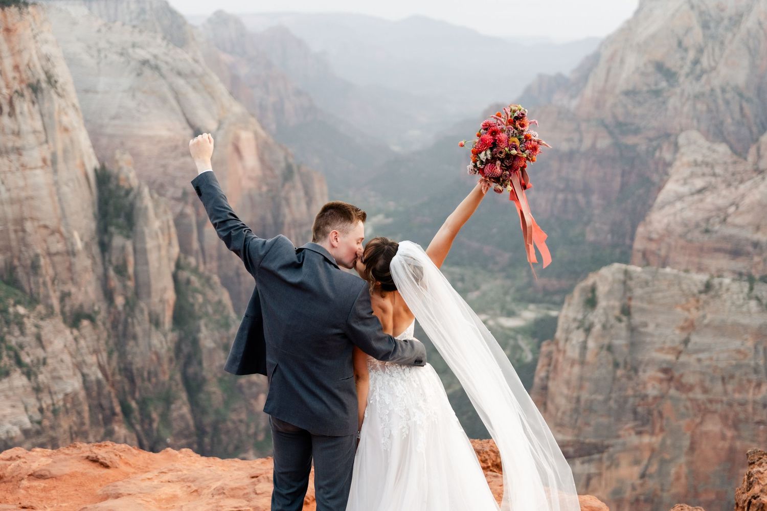 Newlyweds share intimate moments against dramatic mountain backdrop at scenic overlook in Zion National Park. Zion wedding photographer.
