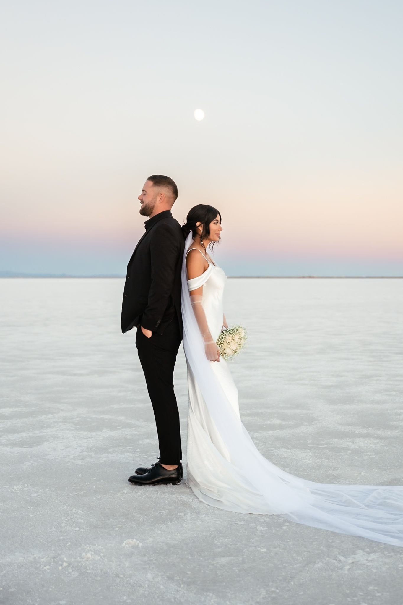 Bride and groom pose dramatically on salt flats with flowing white dress.