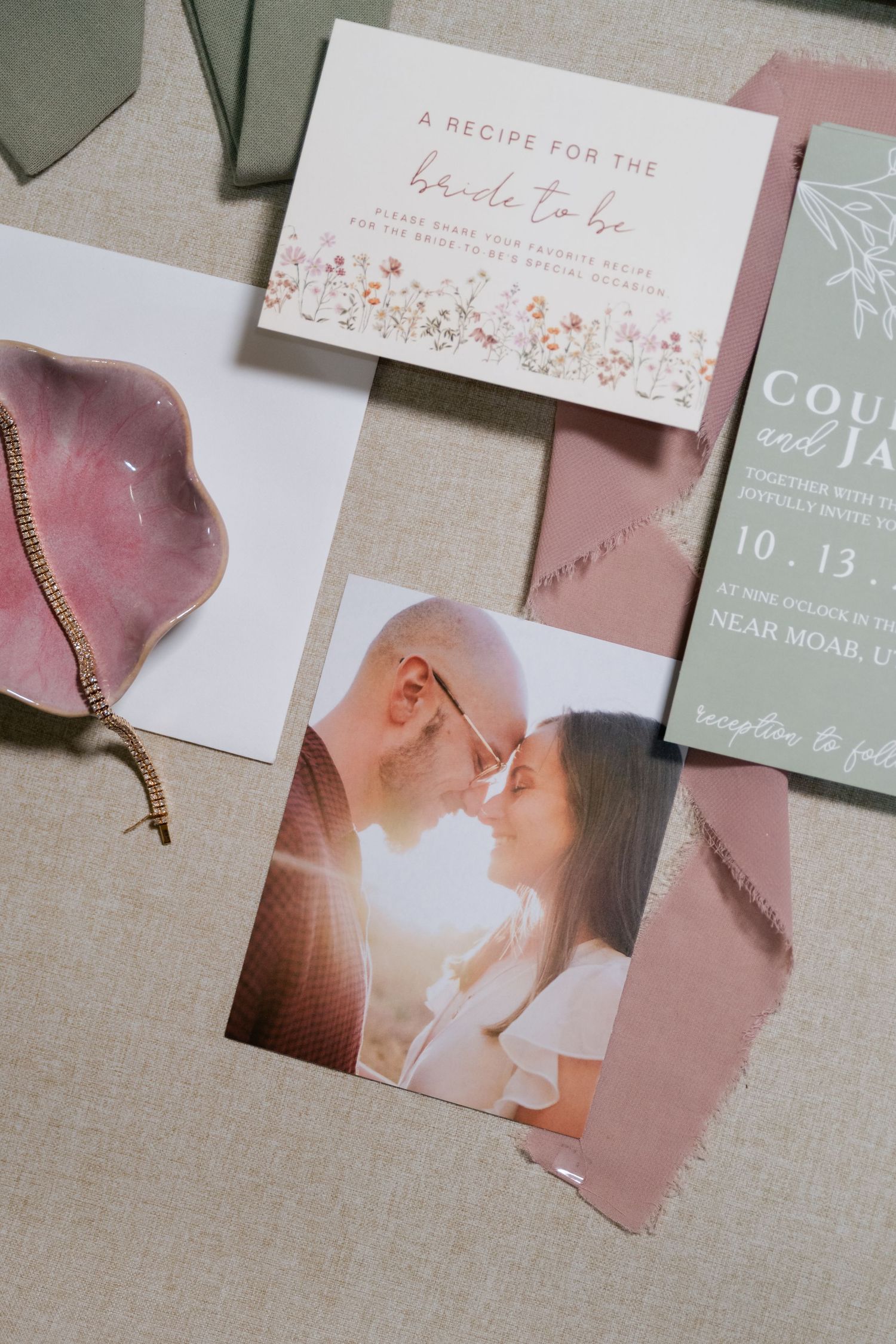 Wedding stationery and invitations in soft pink and gray tones laid out on a neutral linen background.