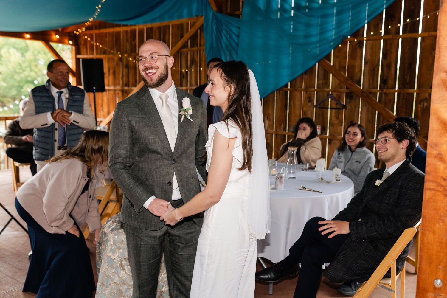 Wedding reception guests mingle and dance under string lights in a rustic wooden pavilion.