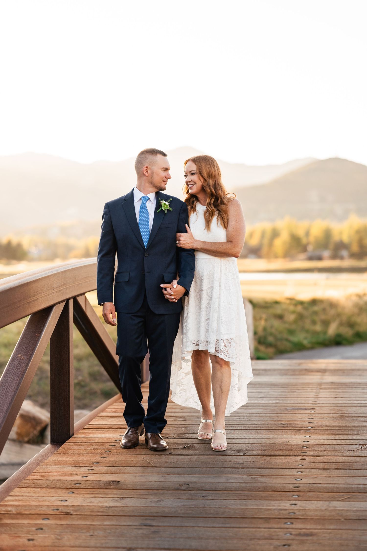 Couple shares intimate moment on wooden boardwalk with mountain landscape in background at sunset.