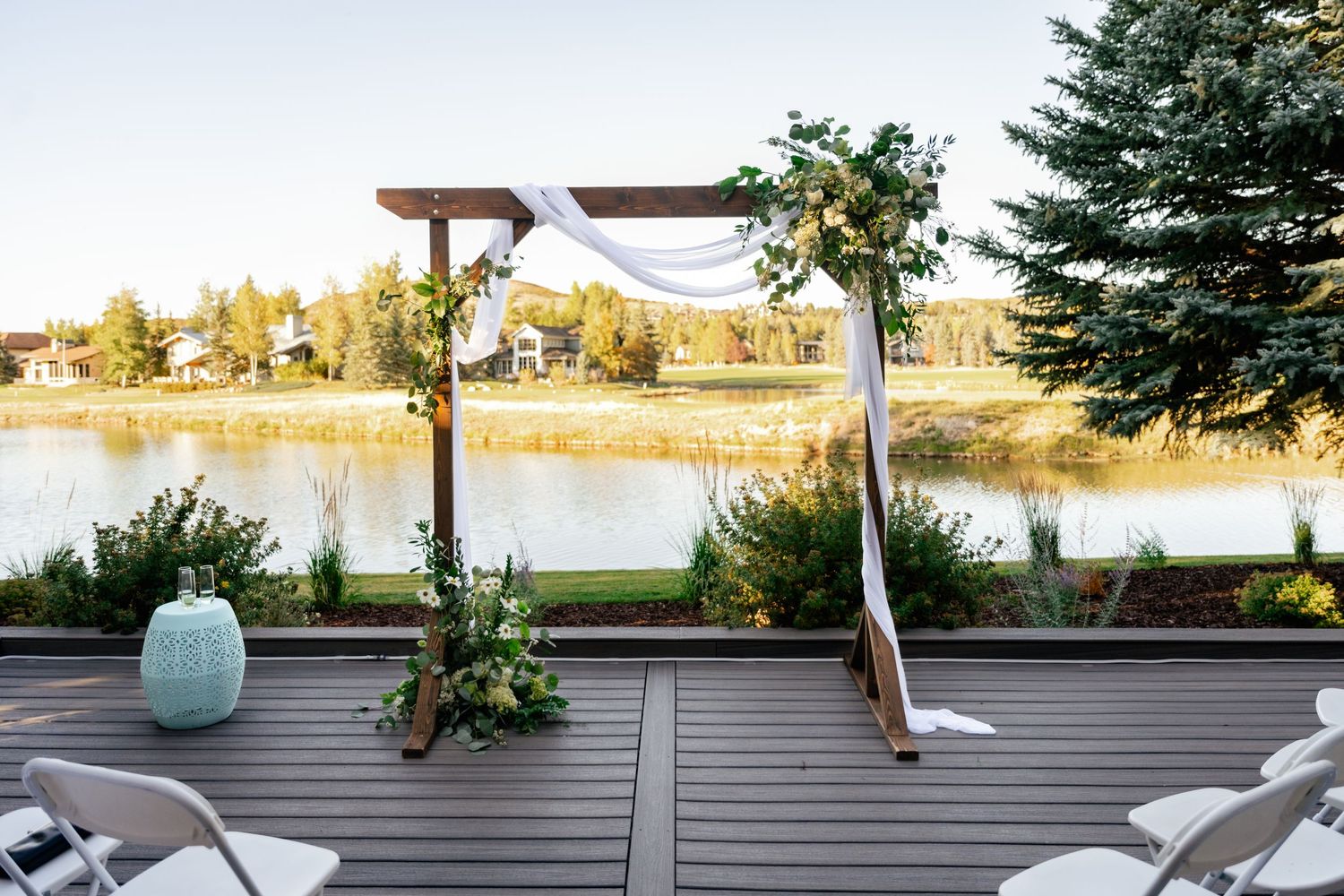 Wedding guests enjoying a casual outdoor reception on a wooden deck with mountain views at sunset.